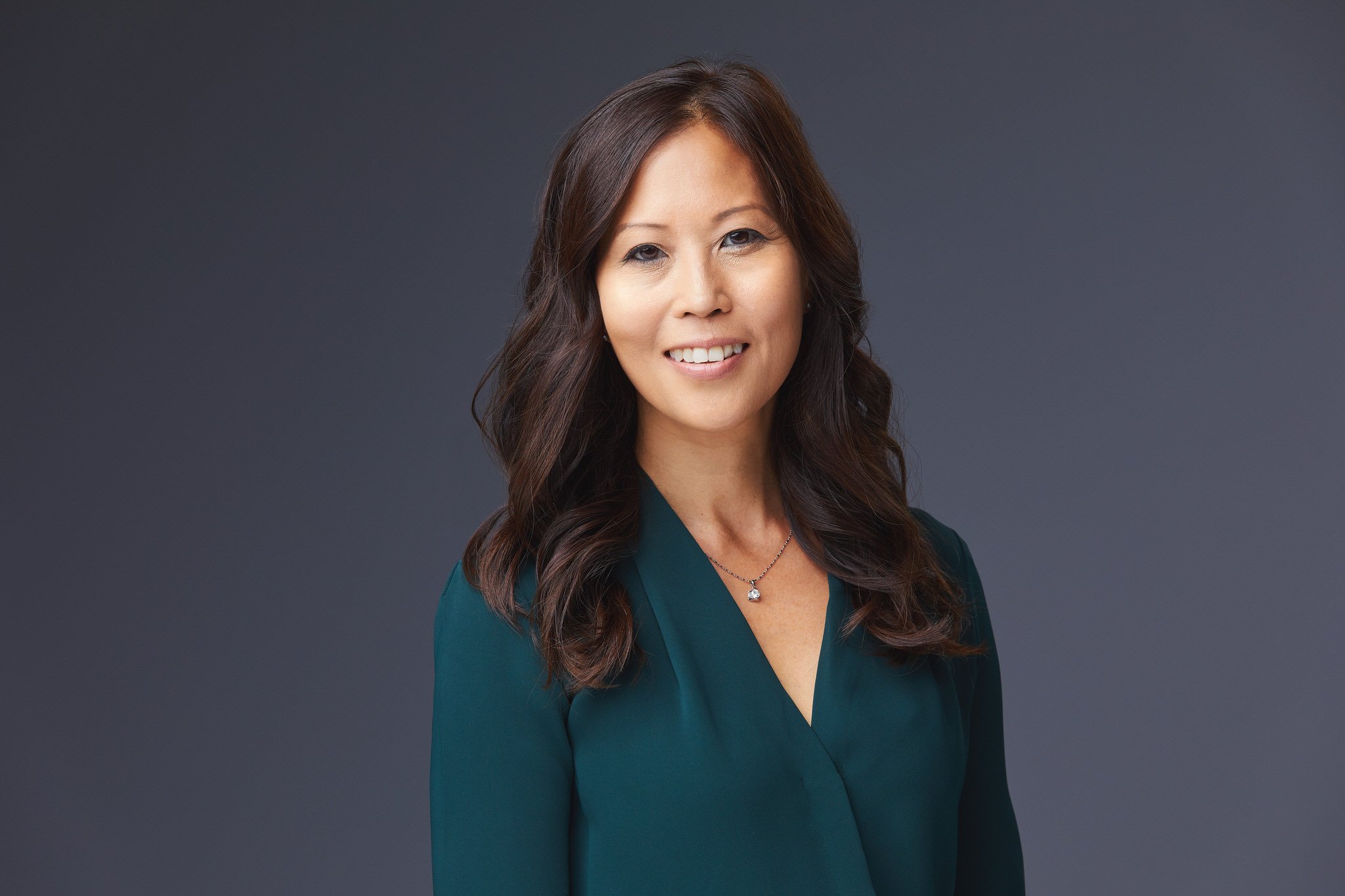 Professional headshot of Katie in a teal blouse against a dark studio background.