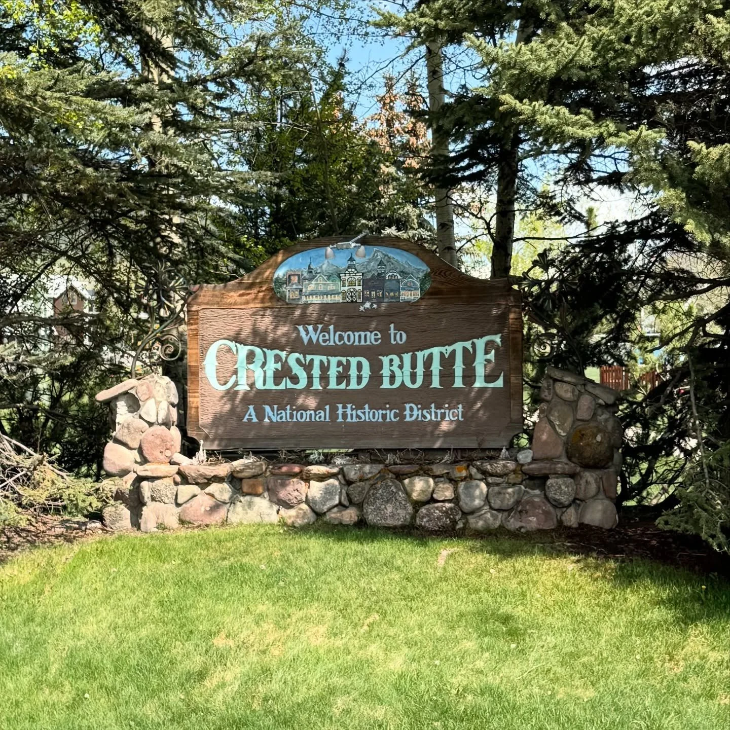 Wooden welcome sign for Crested Butte, a National Historic District, surrounded by rocks and trees.