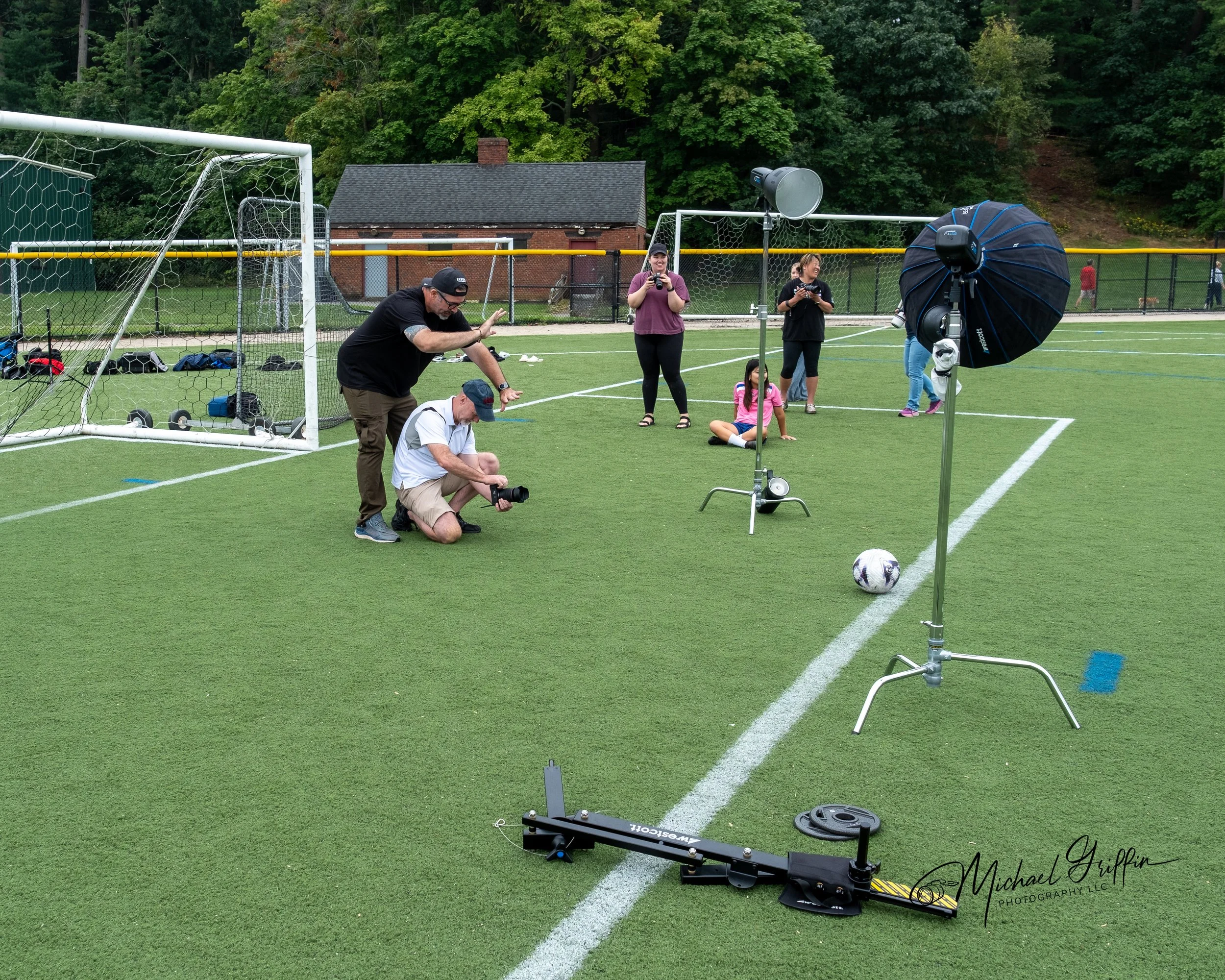 Photo shoot setup on a soccer field with photographers, lighting equipment, and a soccer ball.