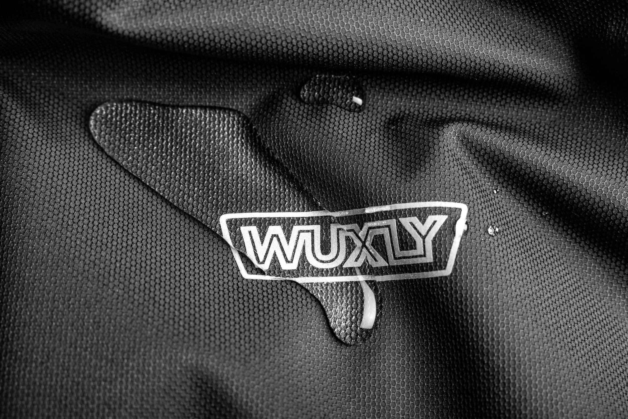 Close-up of a black textured fabric with a white logo reading 'WUXLY' on it.