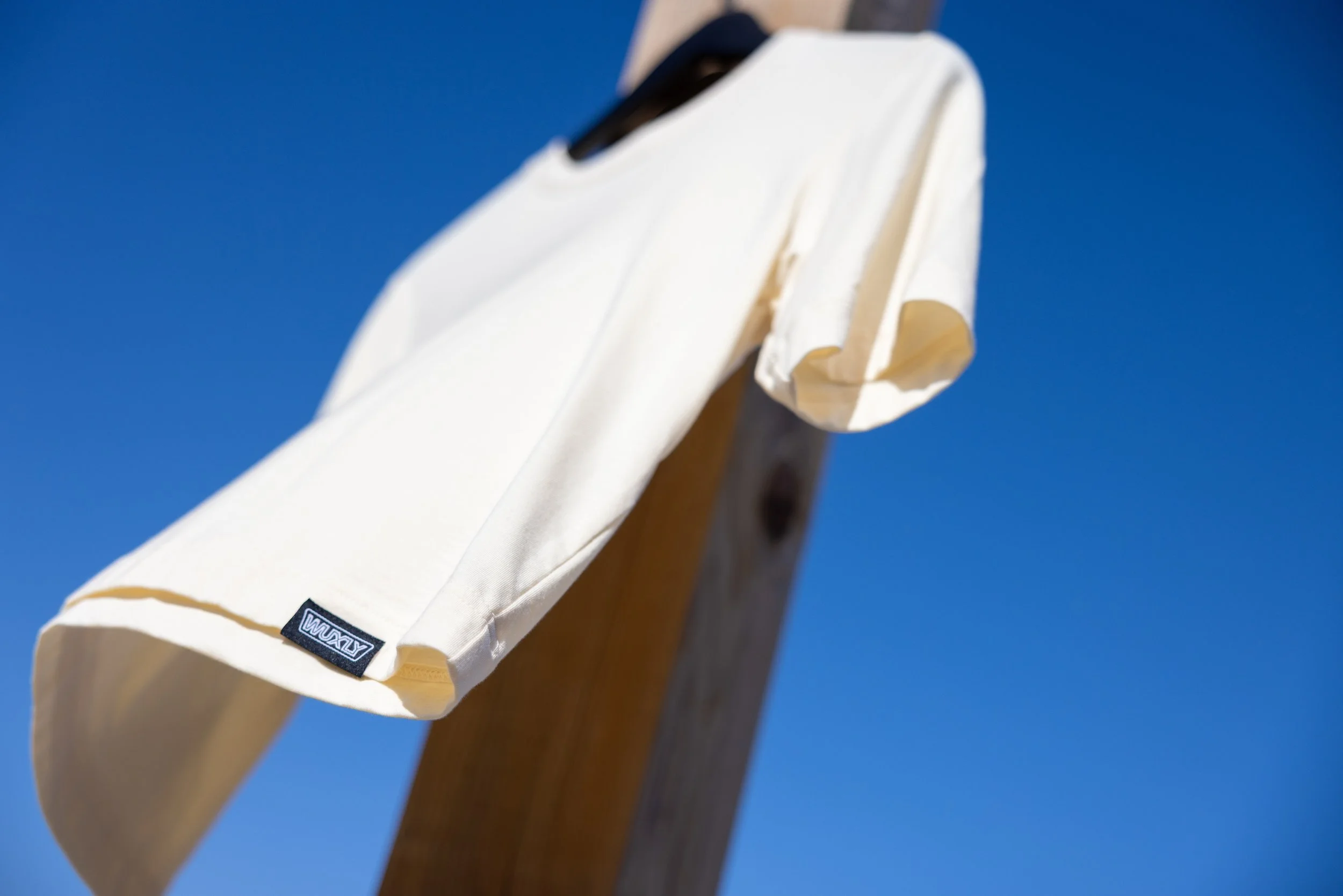 A white T-shirt hanging on a wooden post against a clear blue sky.