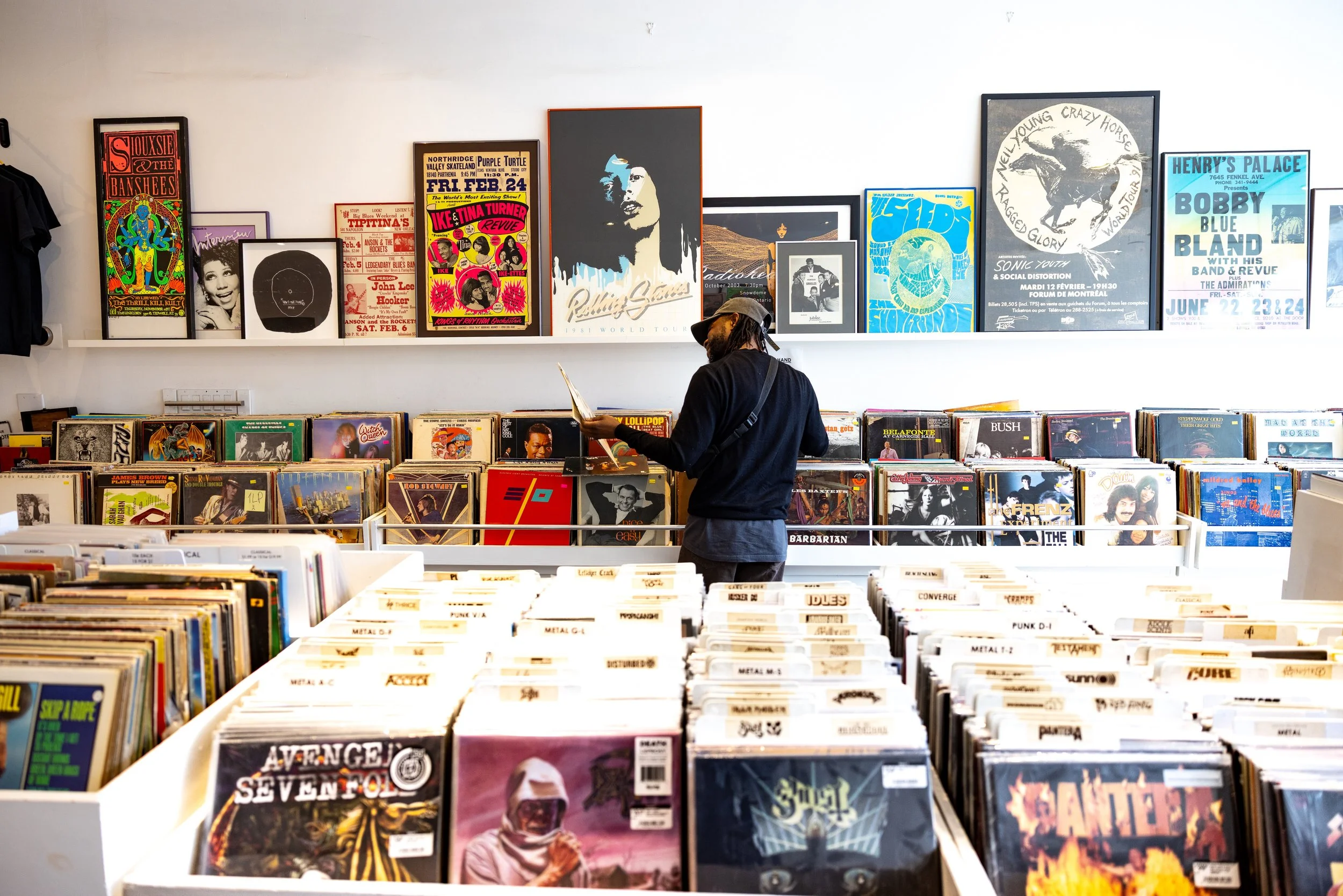 Person browsing vinyl records in a record store with album covers and posters on the wall.