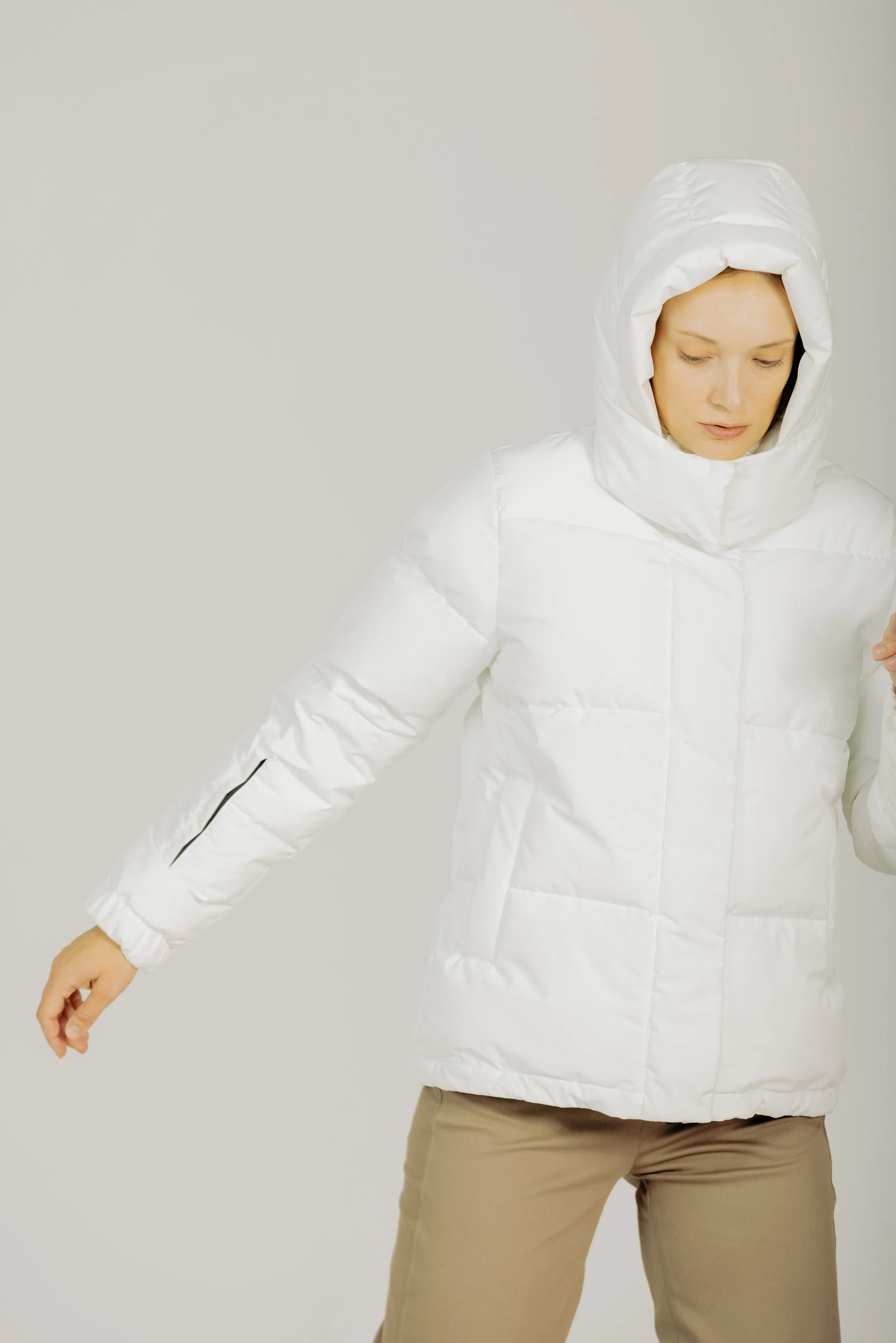 A woman wearing a white puffer jacket with a hood, standing against a plain background.