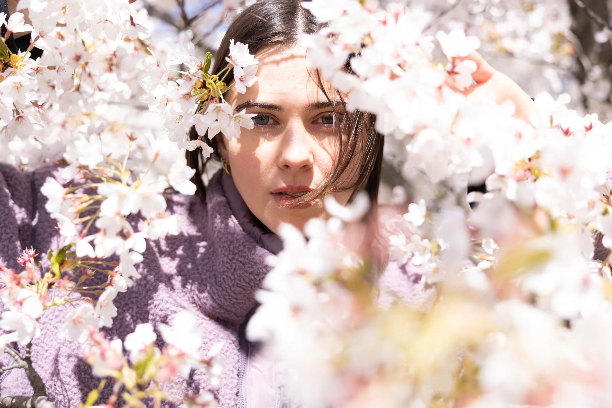 A woman with dark hair and light skin surrounded by blooming cherry blossom flowers.