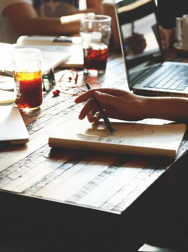 An individual is working with colleagues to write new information at a table
