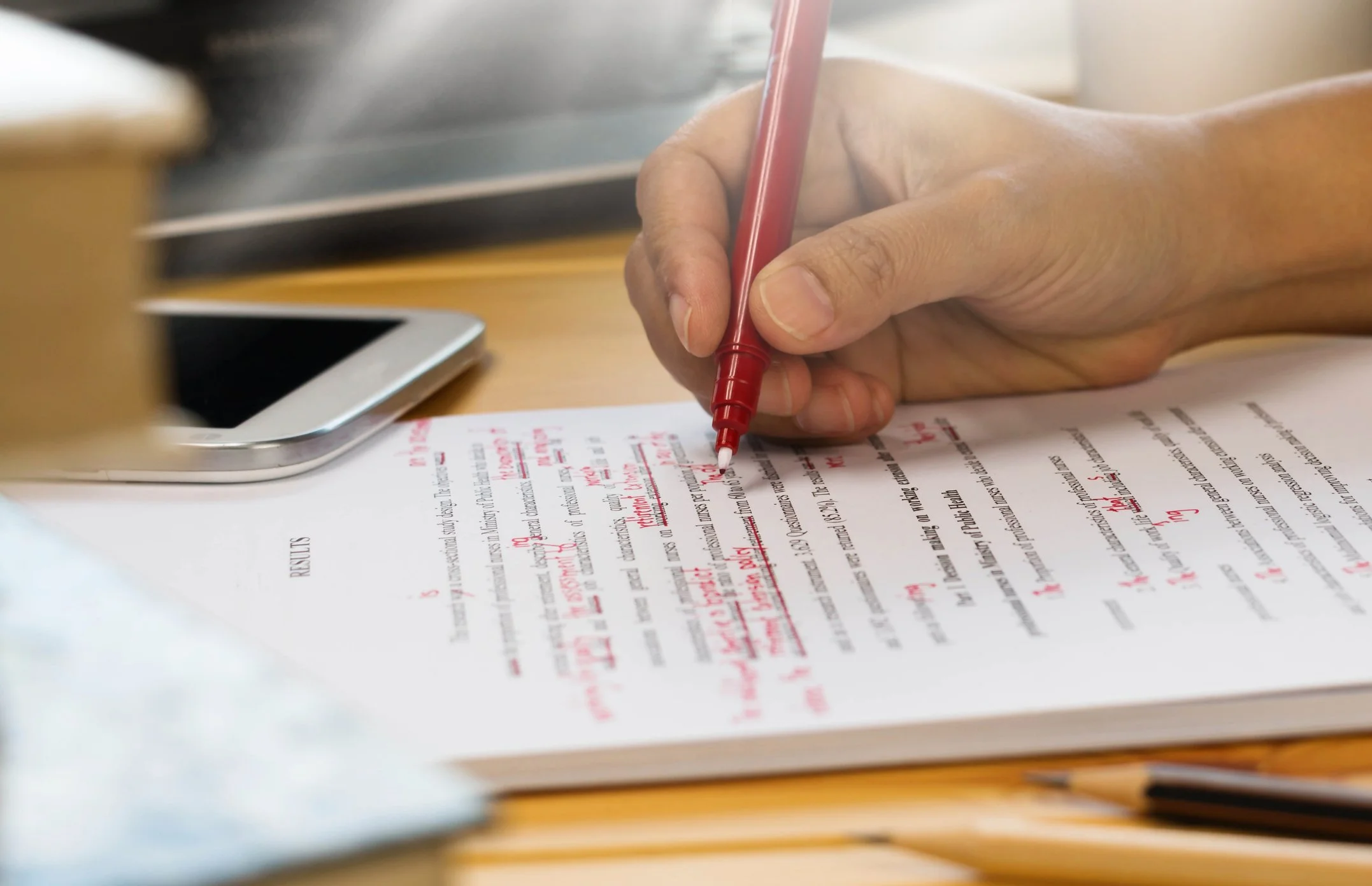 An individual edits text on paper with a red pen