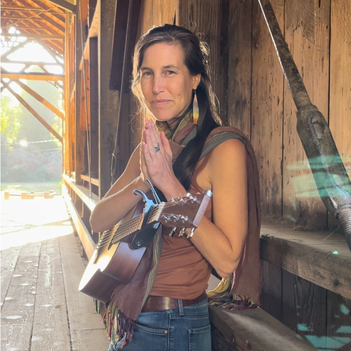 Amanda West with her guitar inside a wooden covered bridge.