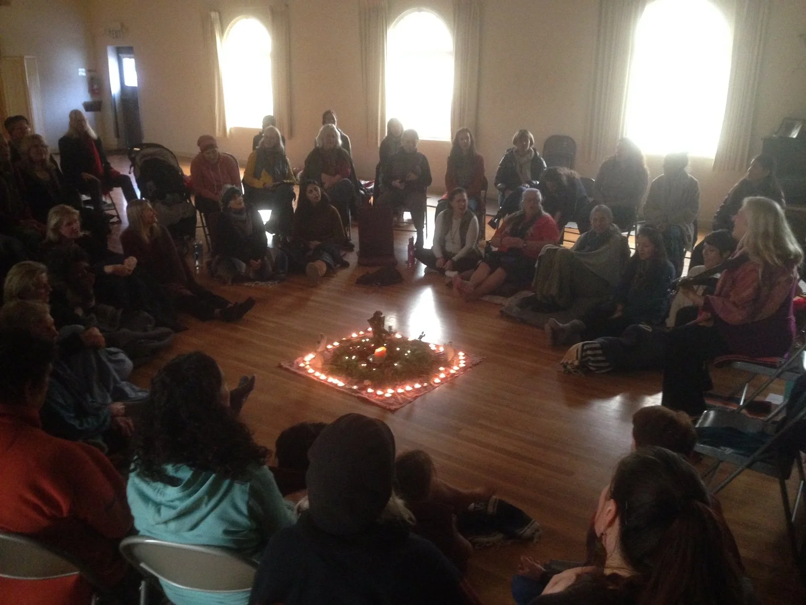 Community singing circle gathered around a candlelit altar.