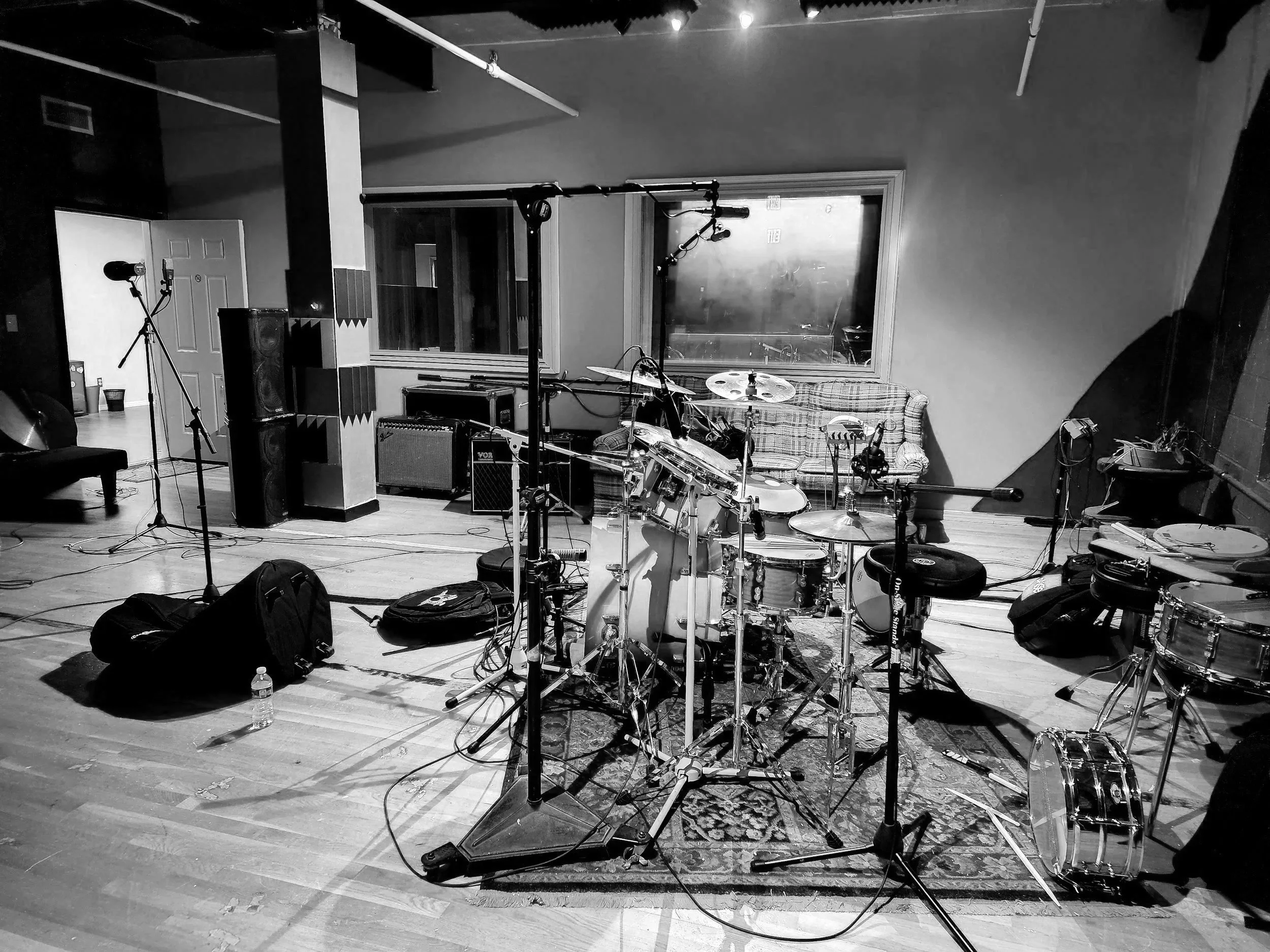 A music recording studio with various instruments including a drum set, microphones, and amplifiers, along with recording equipment and a couch.