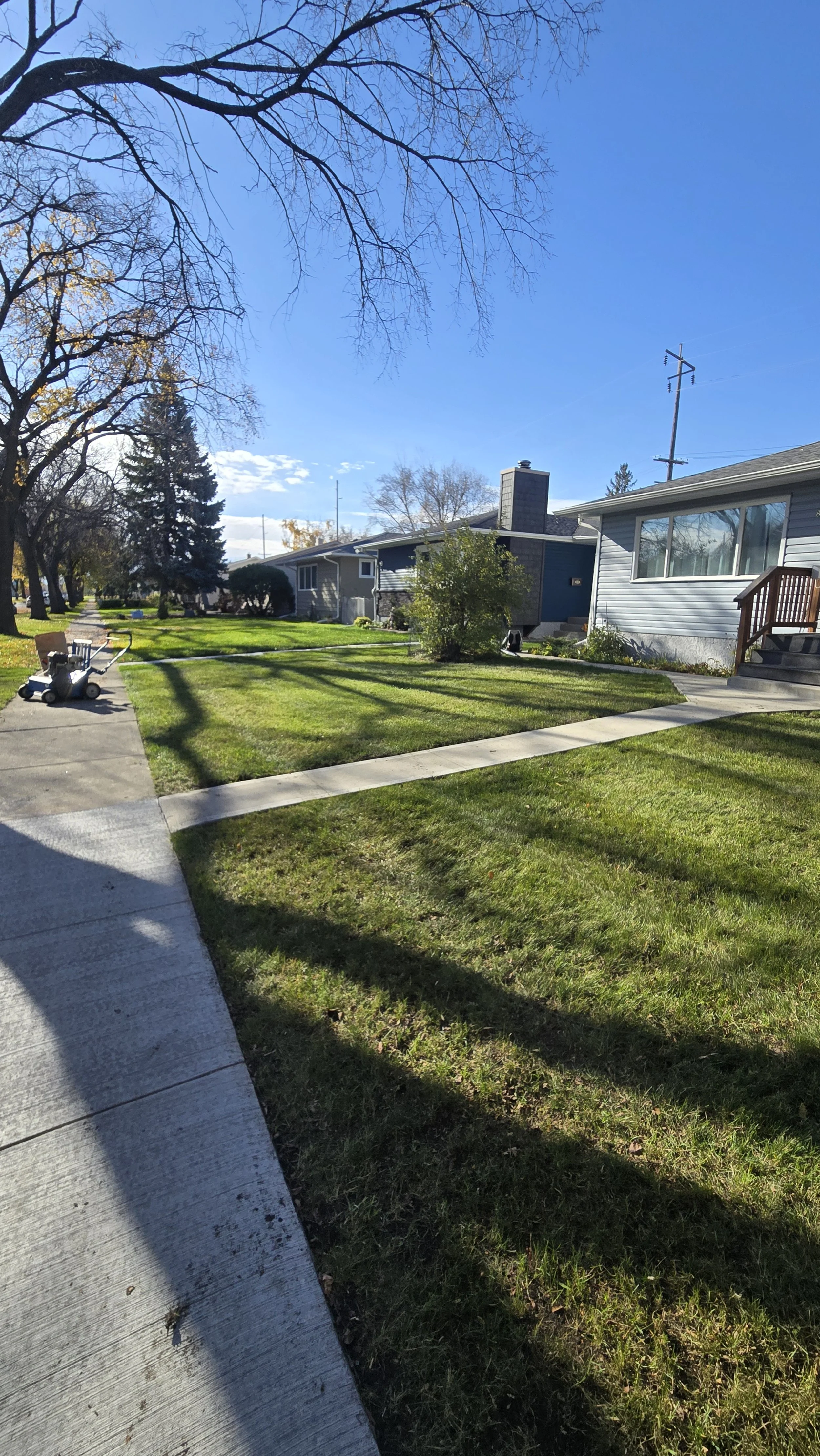 Residential neighborhood with houses, trees, green lawns, and a clear blue sky.