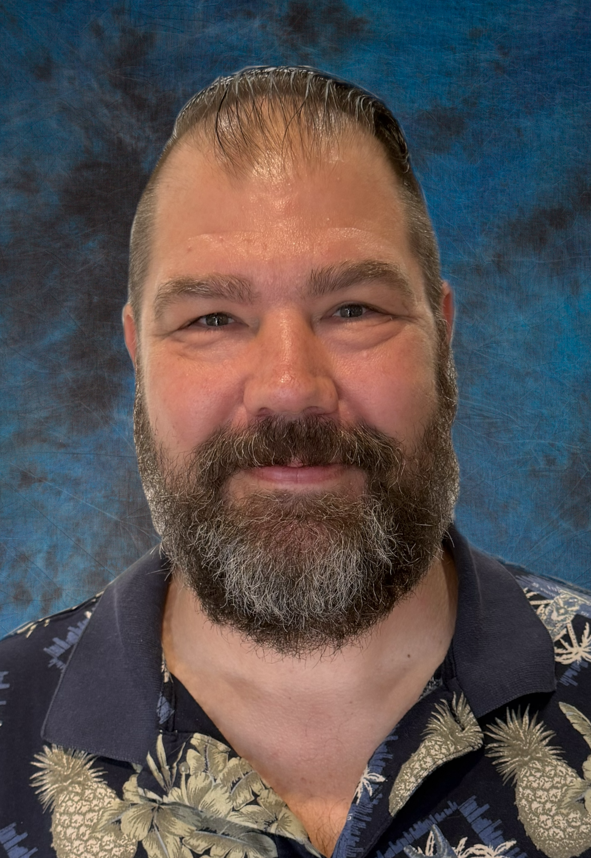 Portrait of a smiling man with short brown hair, wearing a navy blue polo shirt with a church logo, against a dark blue mottled background.