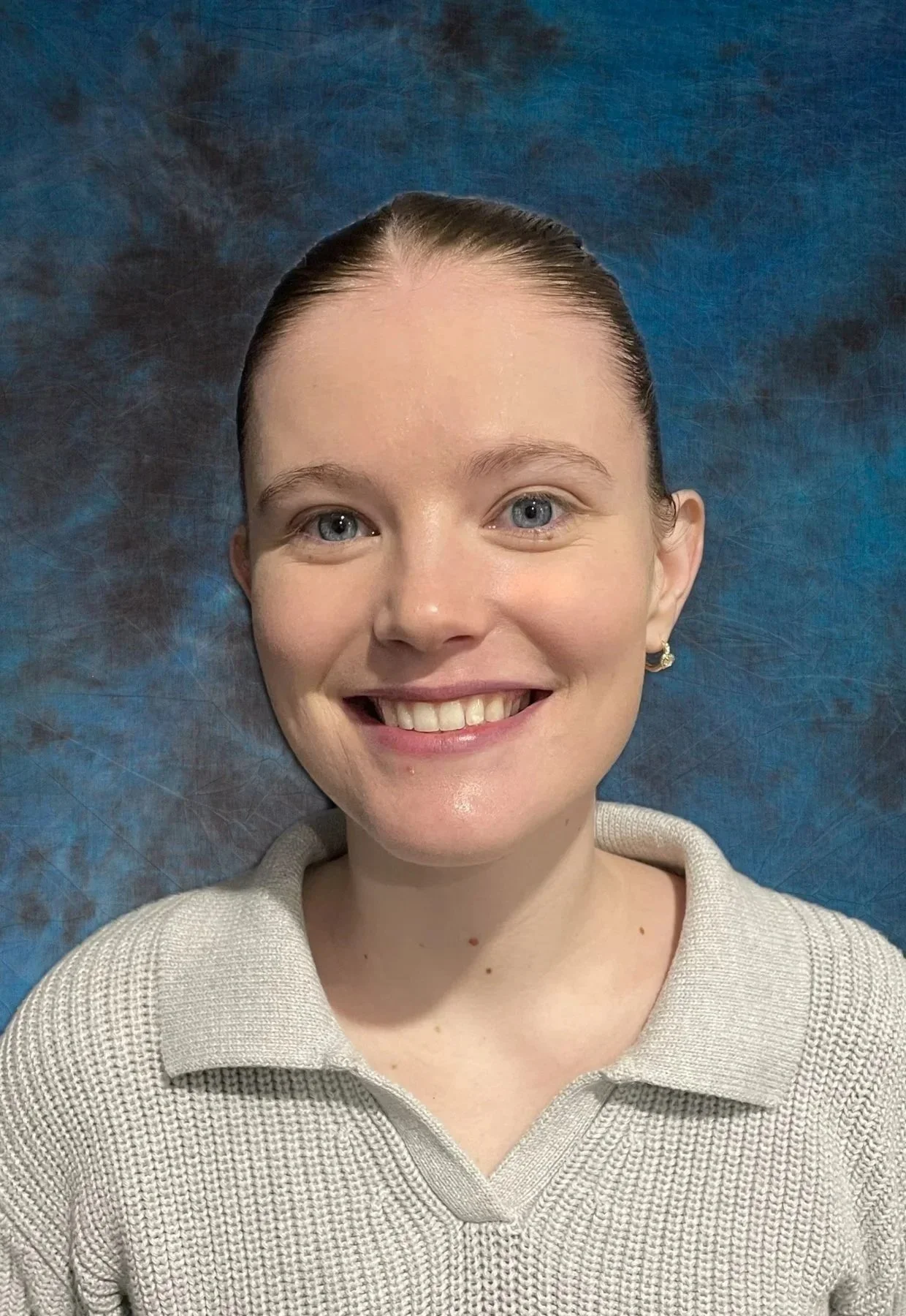 Portrait of a middle-aged woman with long gray hair, wearing pearl earrings and a dark blue top, posed against a textured blue background.