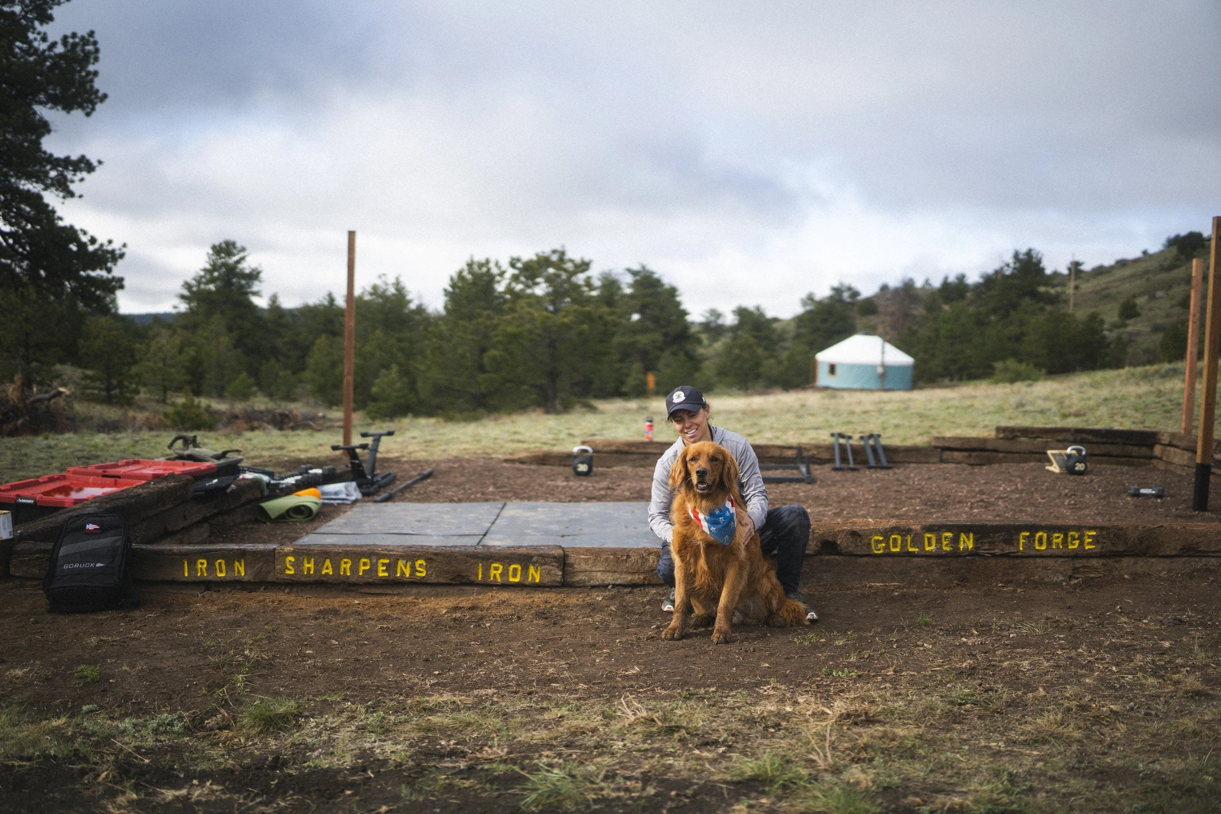 Golden Forge’s founder and dog beside the Iron Sharpens Iron beam in the outdoor training area.