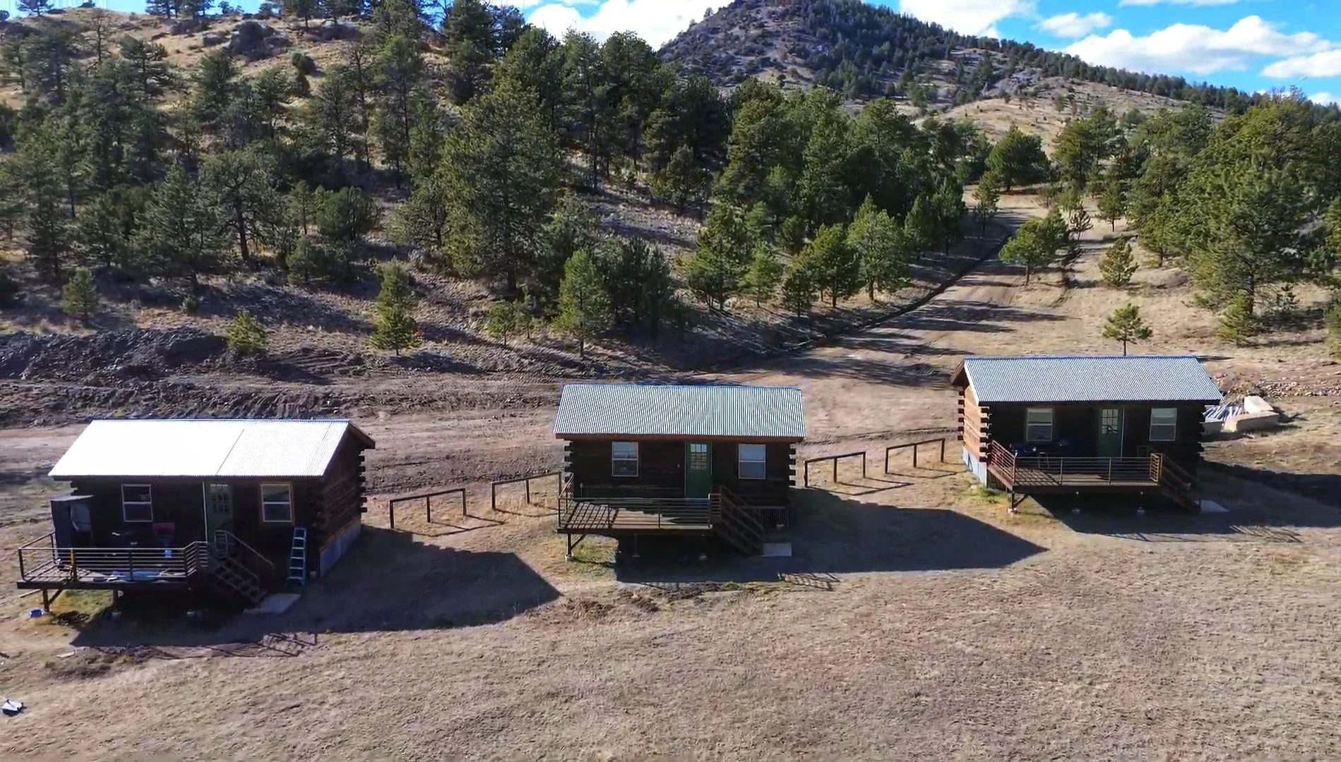 Three log cabins with exterior decks set against a hillside backdrop at Golden Forge