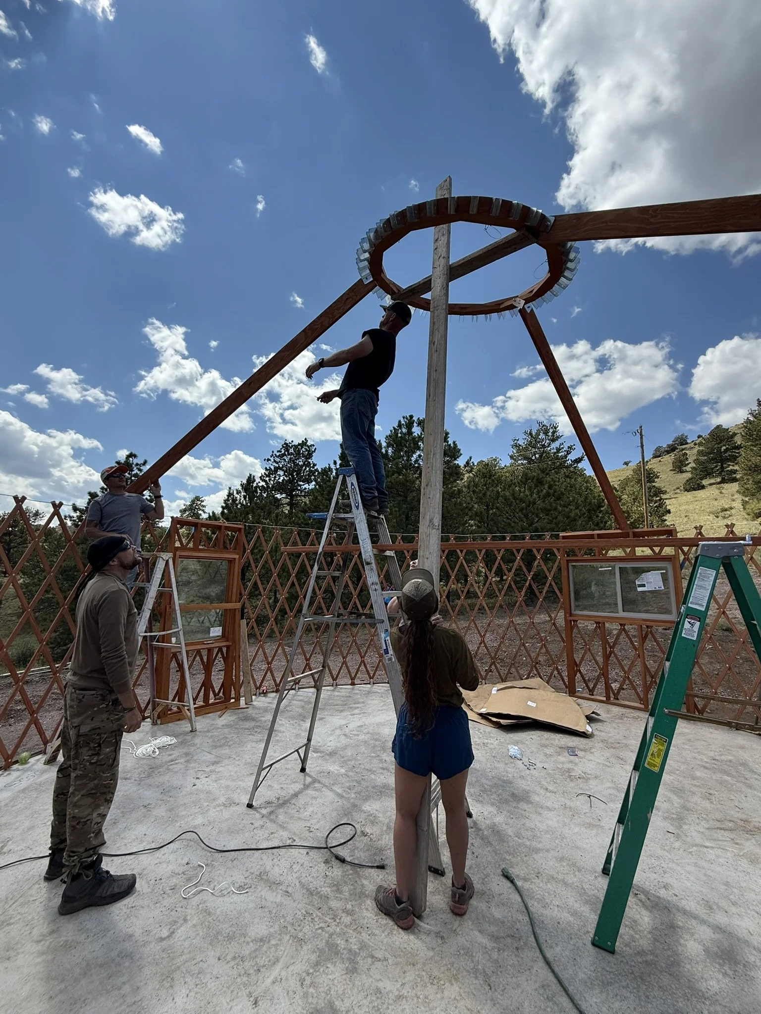 Four people working together to assemble the wooden roof frame of a yurt at Golden Forge.