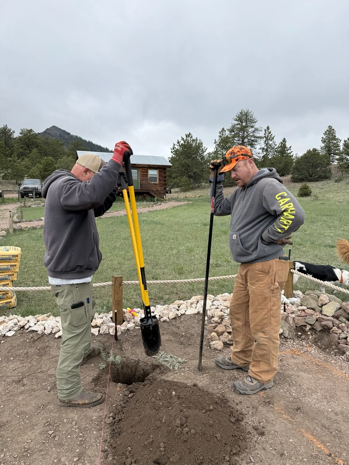 Two people work together digging a posthole at Golden Forge.