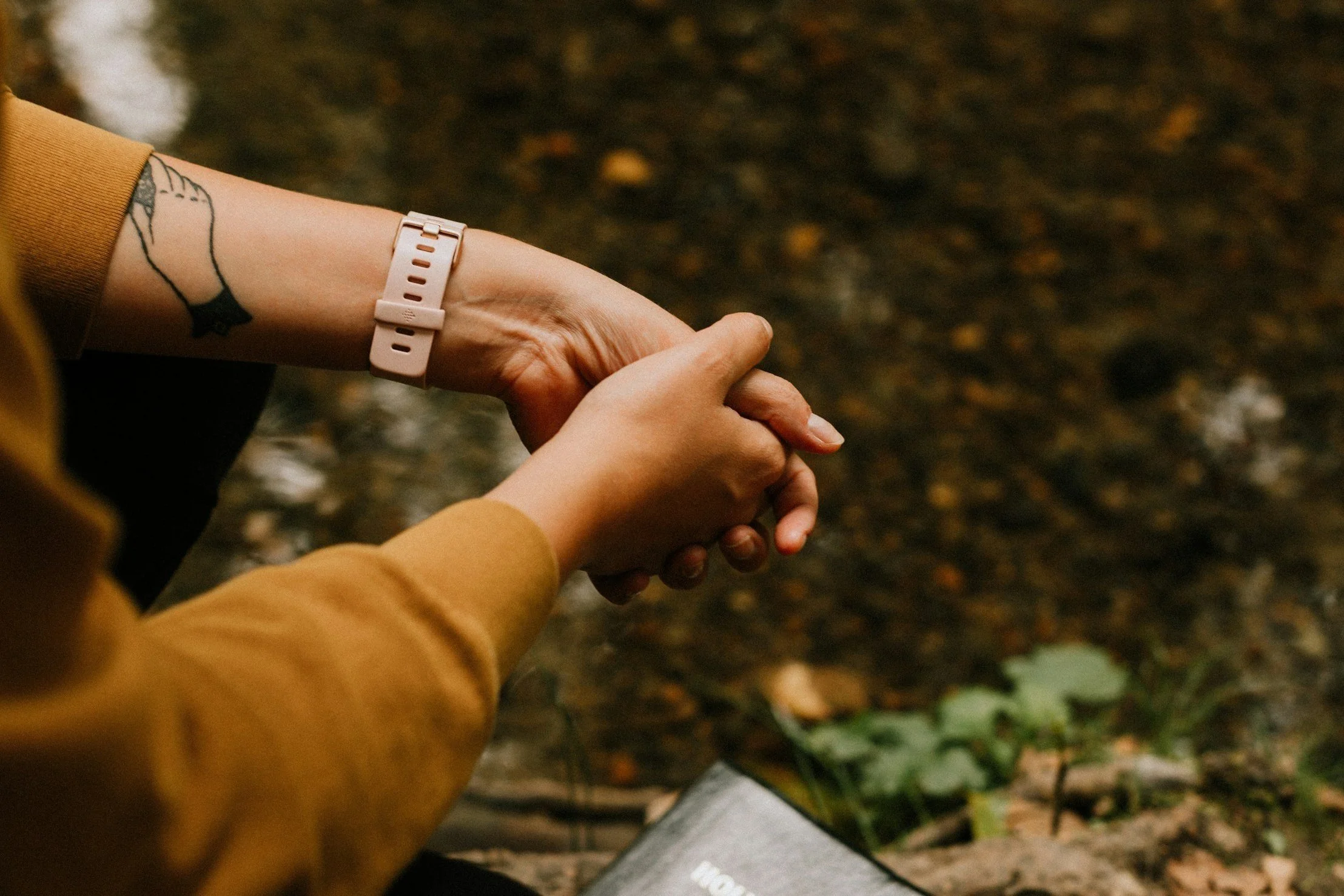 Person with tattoo and smartwatch, clasped hands, outside.