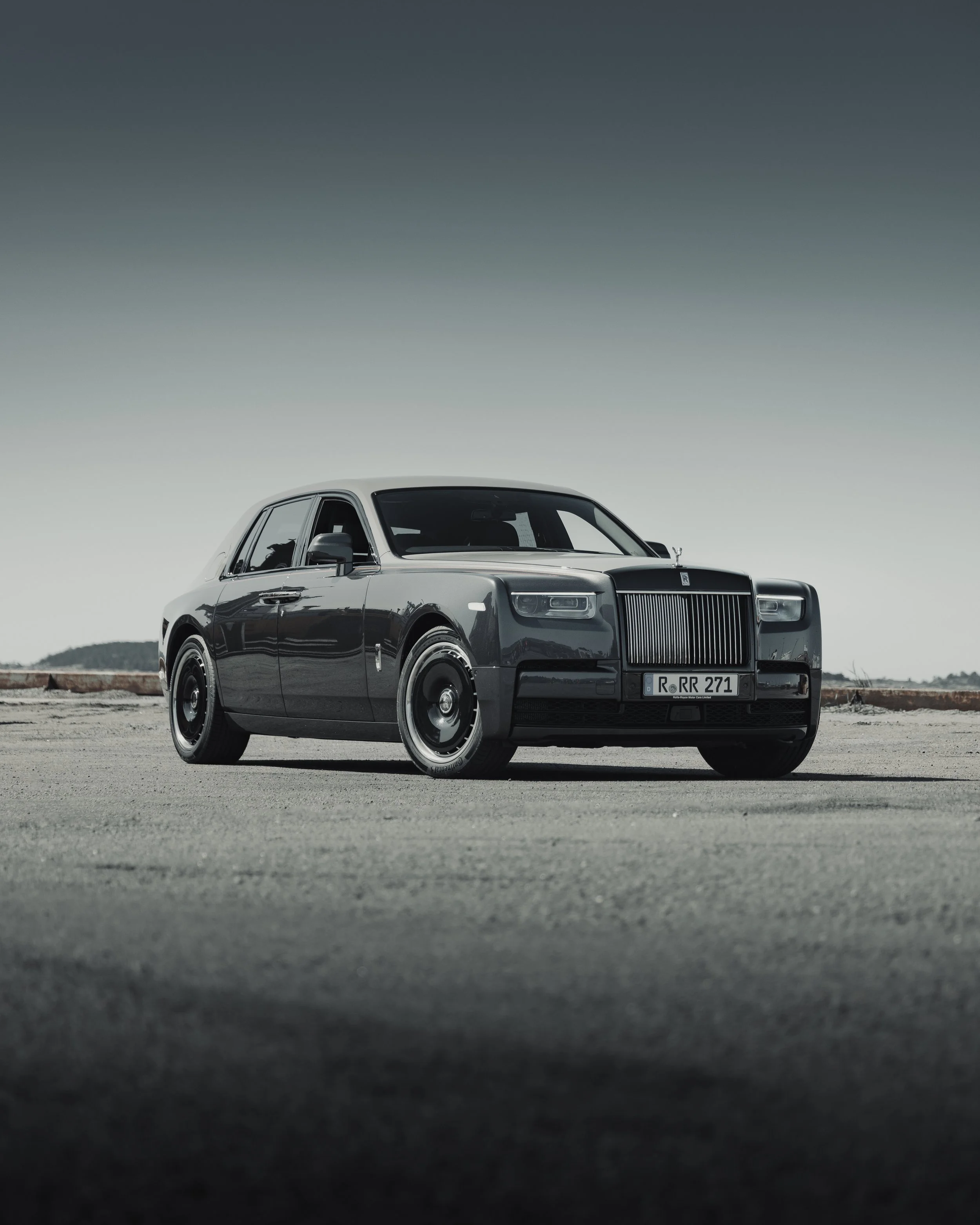 A black luxury Rolls-Royce sedan parked on a flat, open area with an overcast sky in the background.