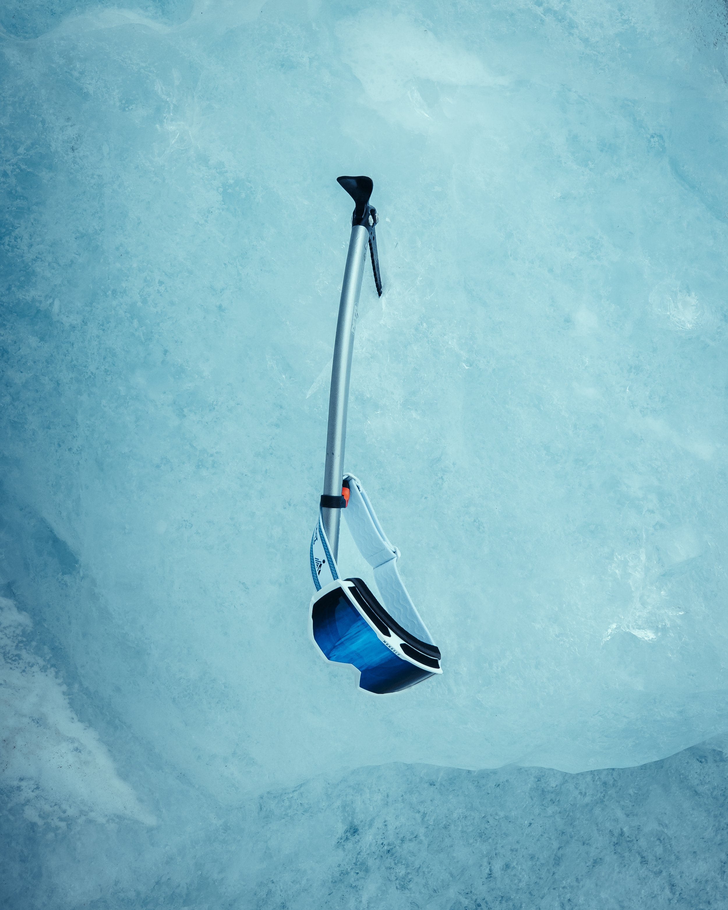 An ice climbing tool with a curved handle and a safety strap, hanging from a snowy or icy surface.