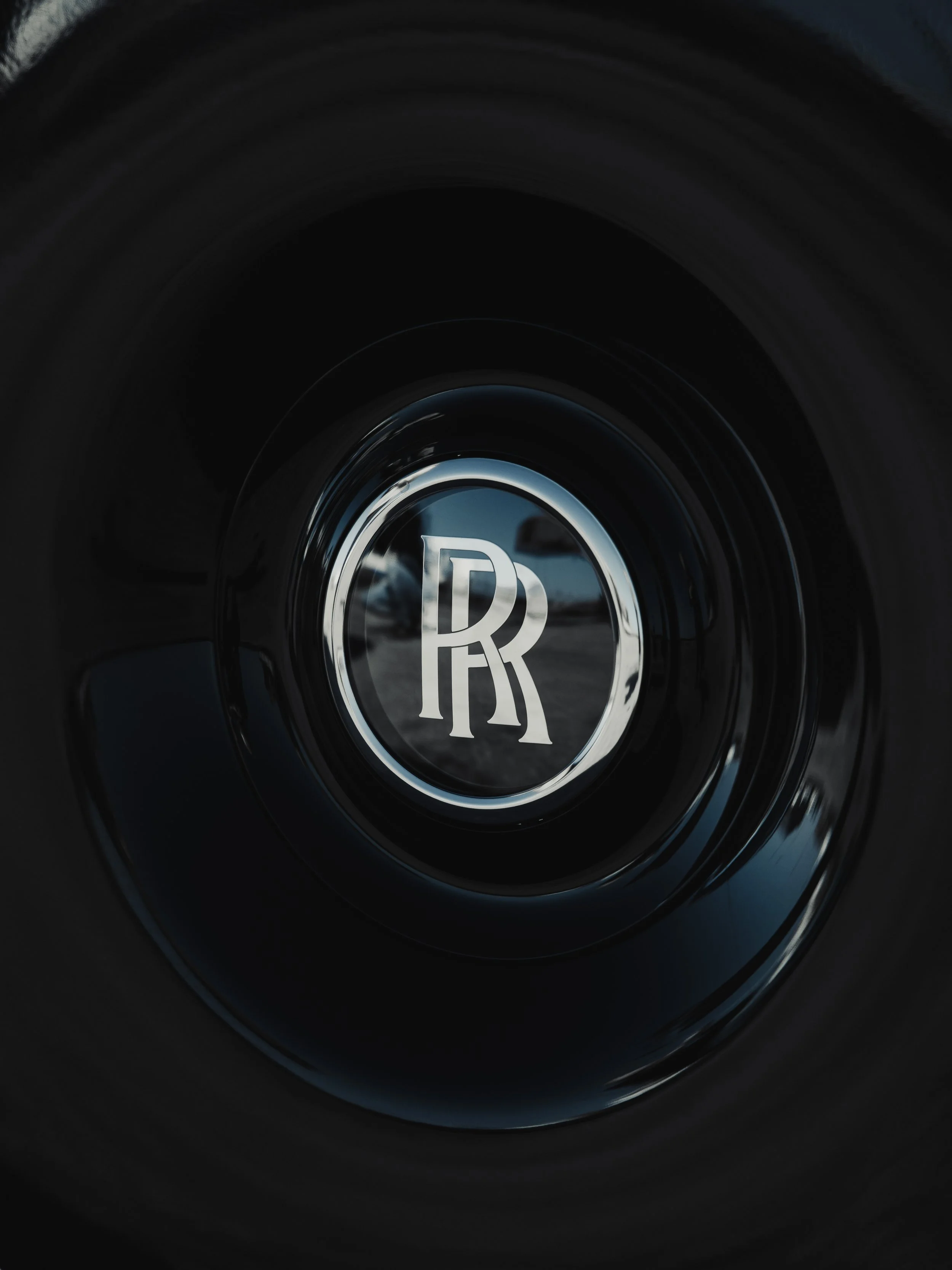 Close-up of a black tire with a shiny silver Rolls-Royce emblem at the center.