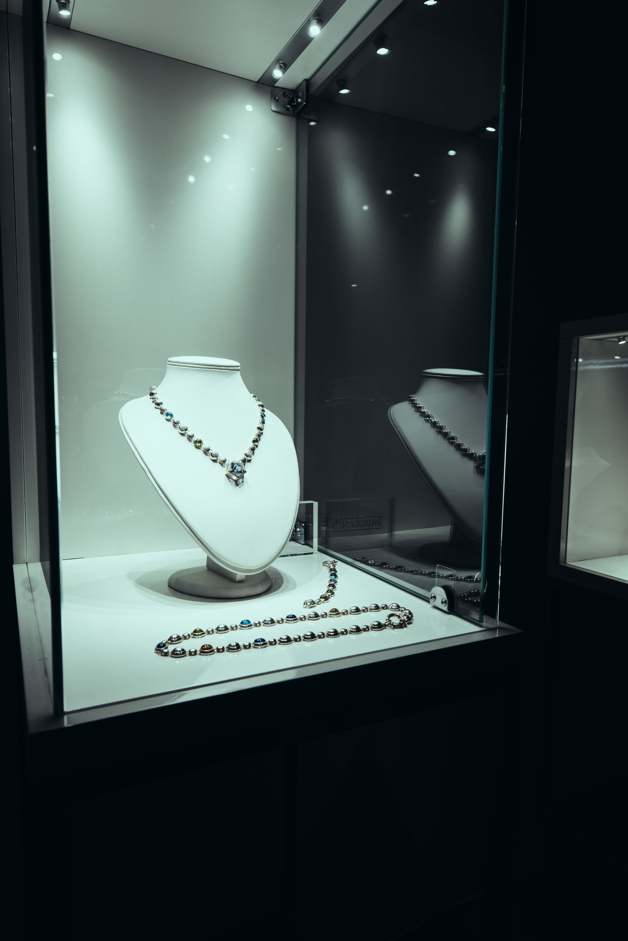 Jewelry display case with a necklace and bracelet on a white bust and surface, with reflections on the glass.