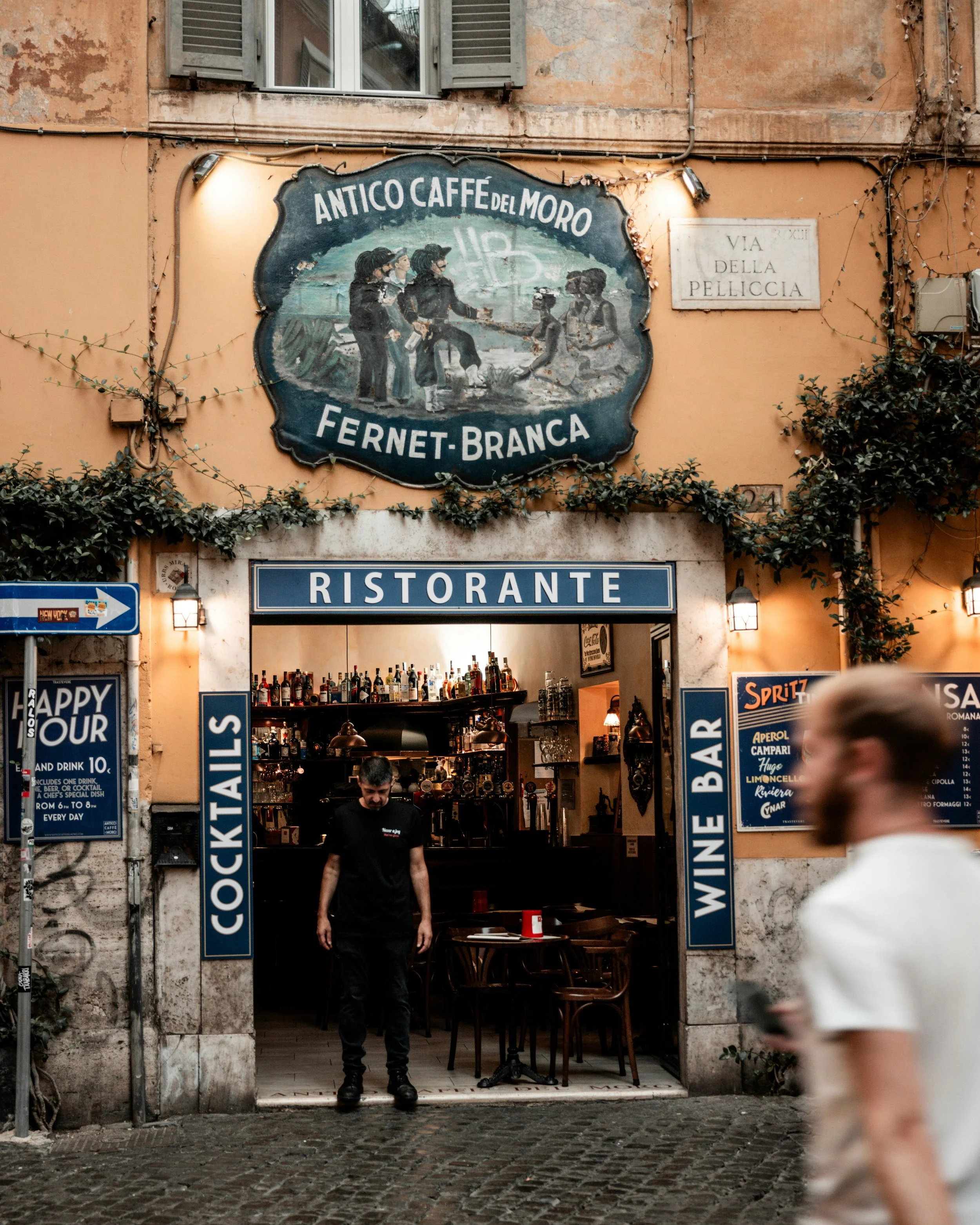 Entrance to Antico Caffè del Moro on Via della Pelliccia in Rome's Trastevere neighborhood, with a vintage Fernet-Branca sign and warm evening lighting