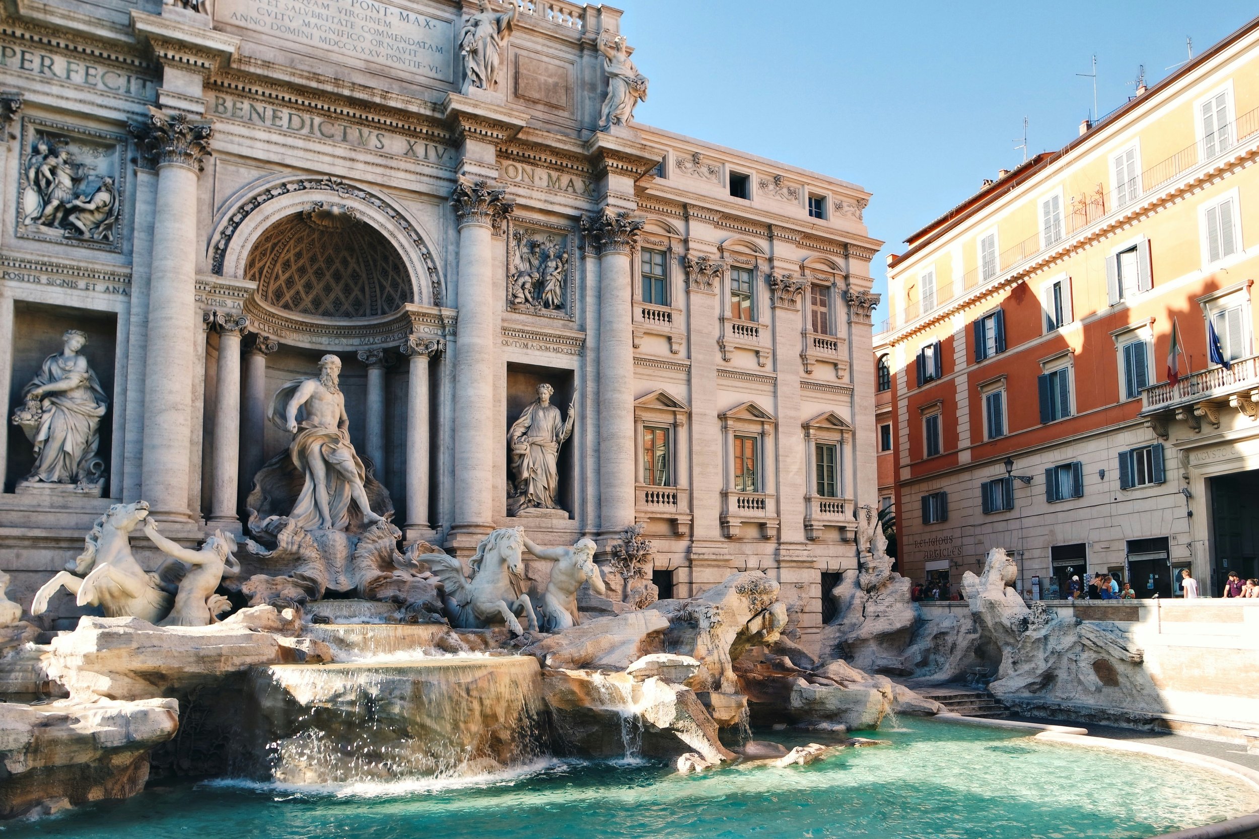 The Trevi Fountain in Rome with its Baroque marble sculptures of Neptune and sea horses in turquoise water on a clear morning