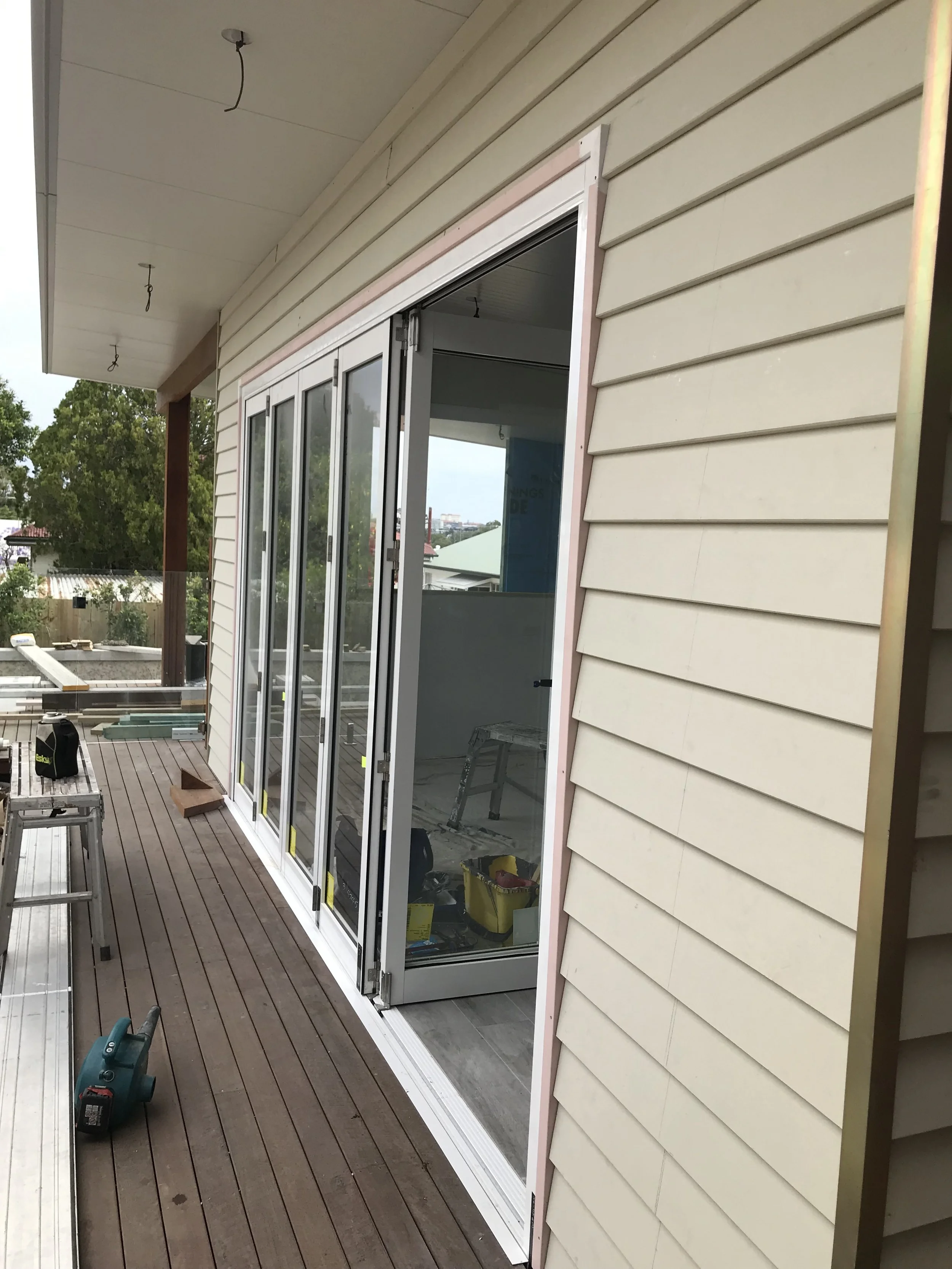 Construction work on a balcony with sliding glass door, tools, and a ladder.