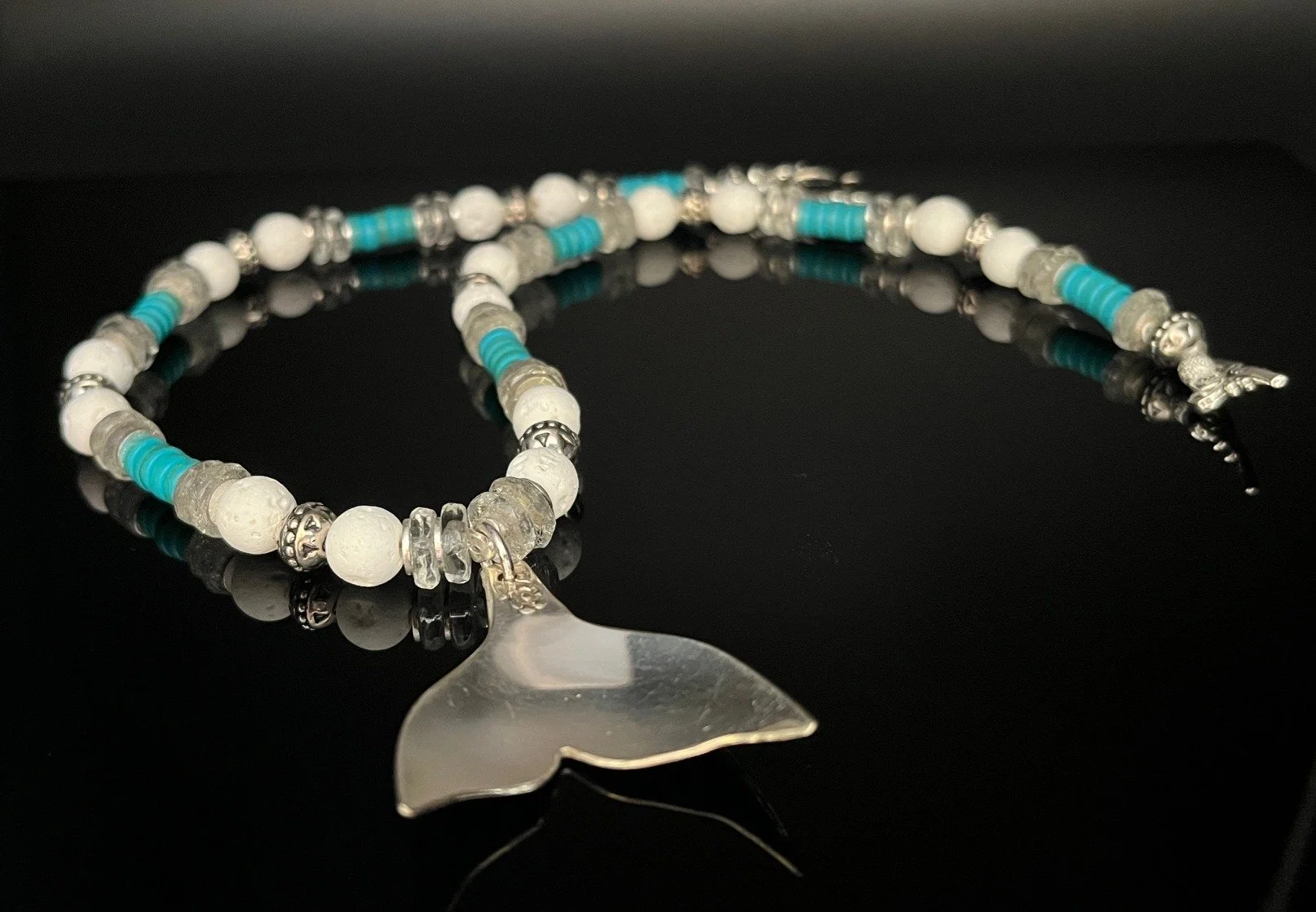 Gold and pale green beaded necklace and bracelet set on a black reflective surface.