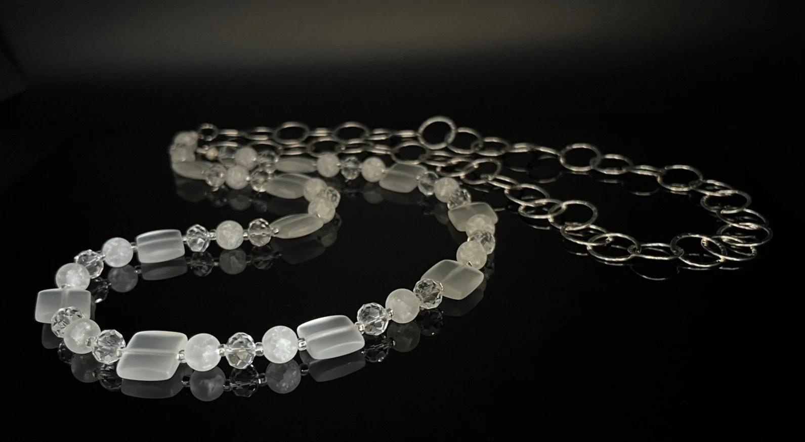 Two pearl necklaces, one with white pearls and blue beads, and one with silver chain links, placed on a black surface.