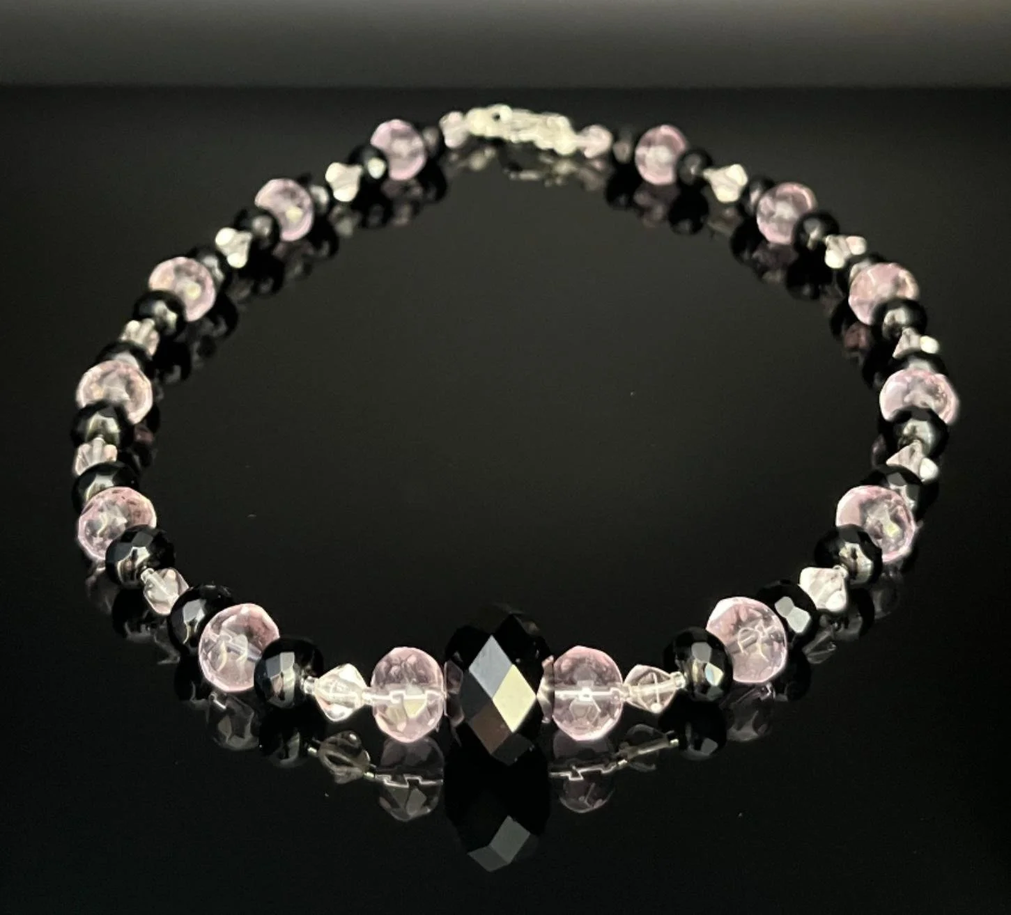 Beaded necklace featuring white pearls, pink beads, silver ornate beads, small teal beads, and a silver clasp, set against a black background.