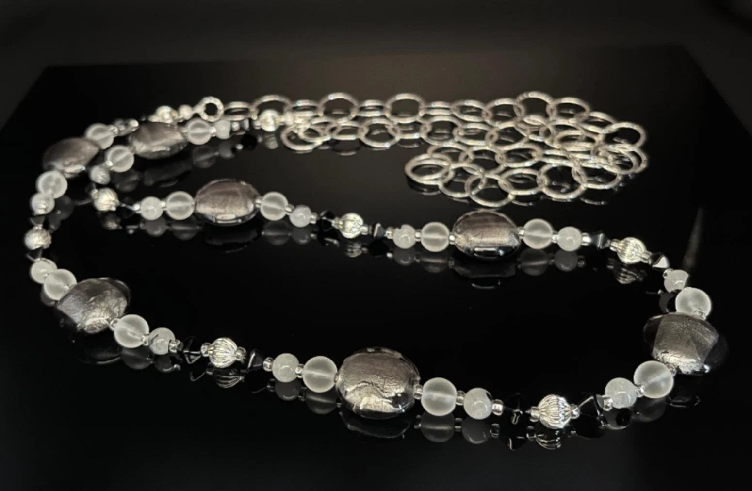 A necklace featuring blue, white, and silver beads with a large silver butterfly pendant on a black background.
