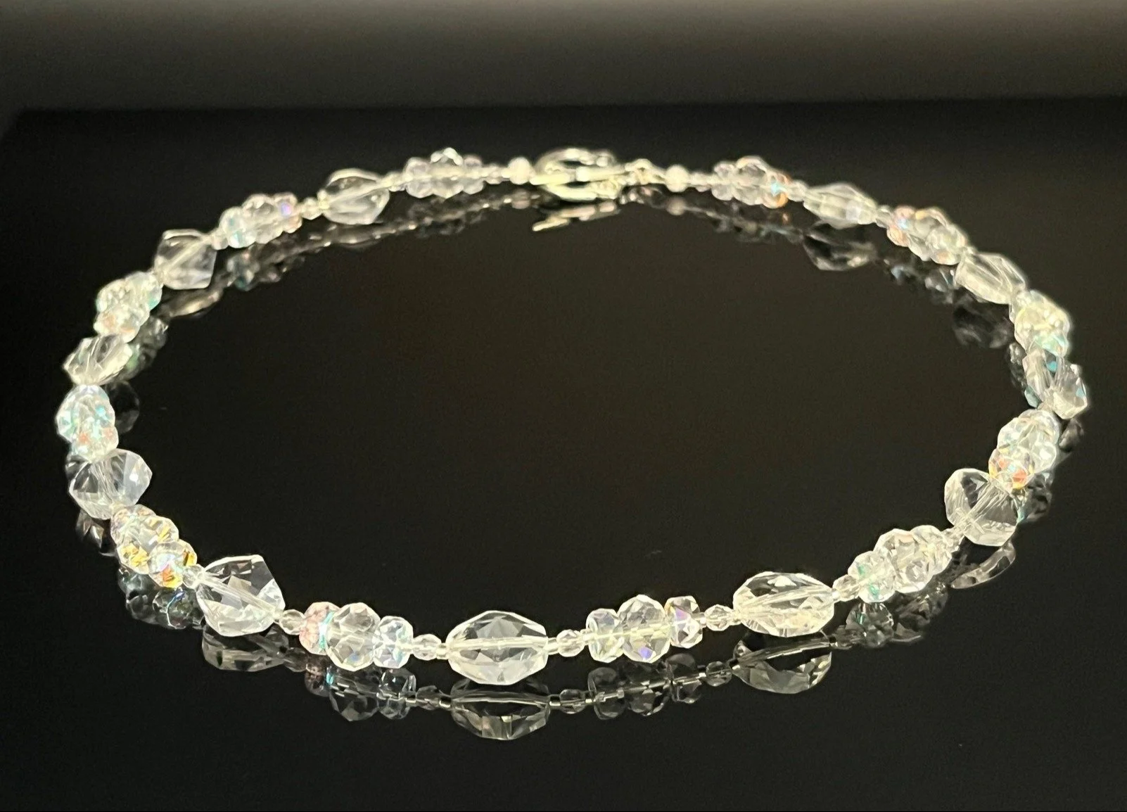 Beaded jewelry necklace with red, white, and clear beads on a black reflective surface.