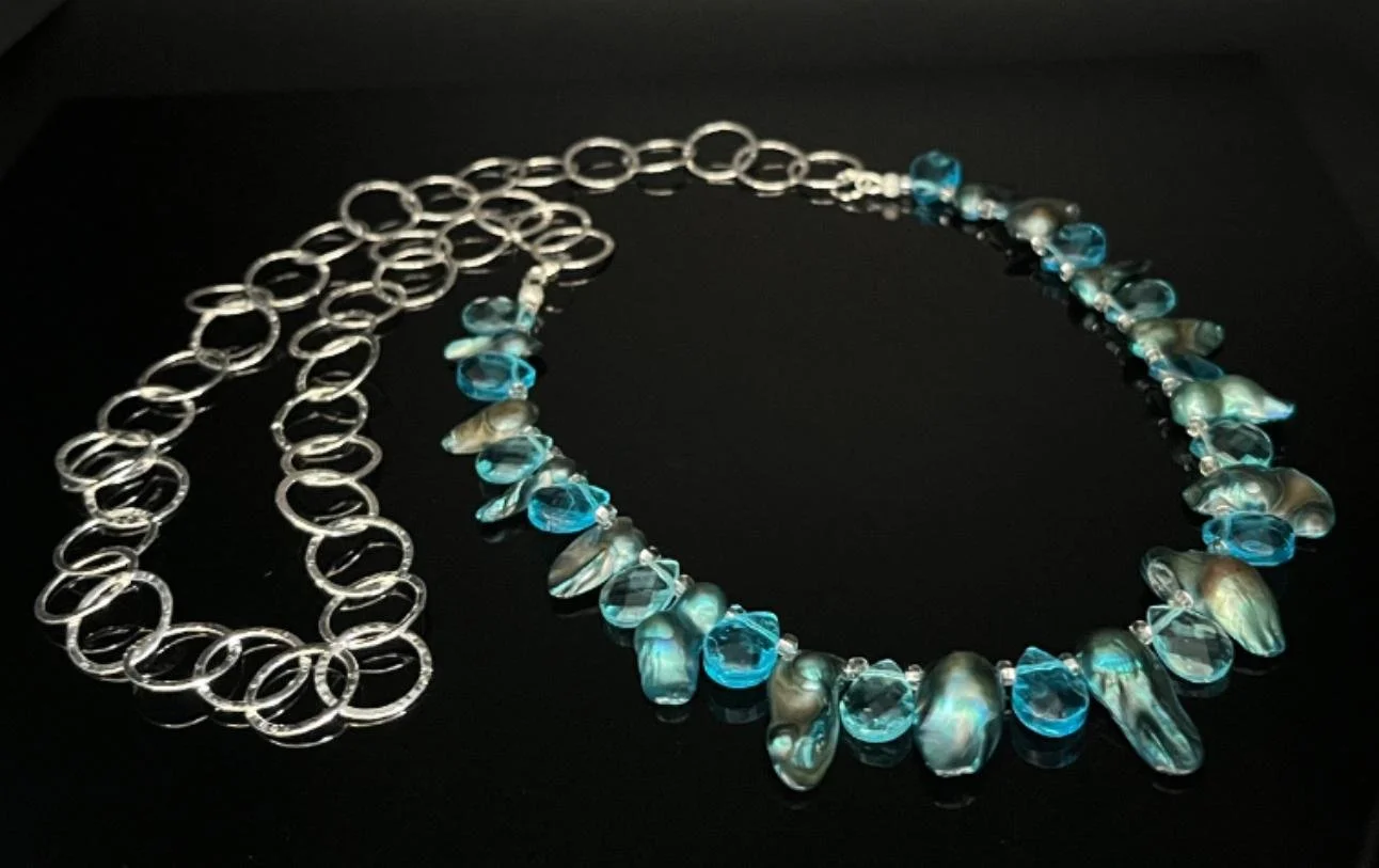 Silver necklace with a chain link design, a heart-shaped pendant, and a teardrop-shaped gemstone at the bottom, displayed against a black background.