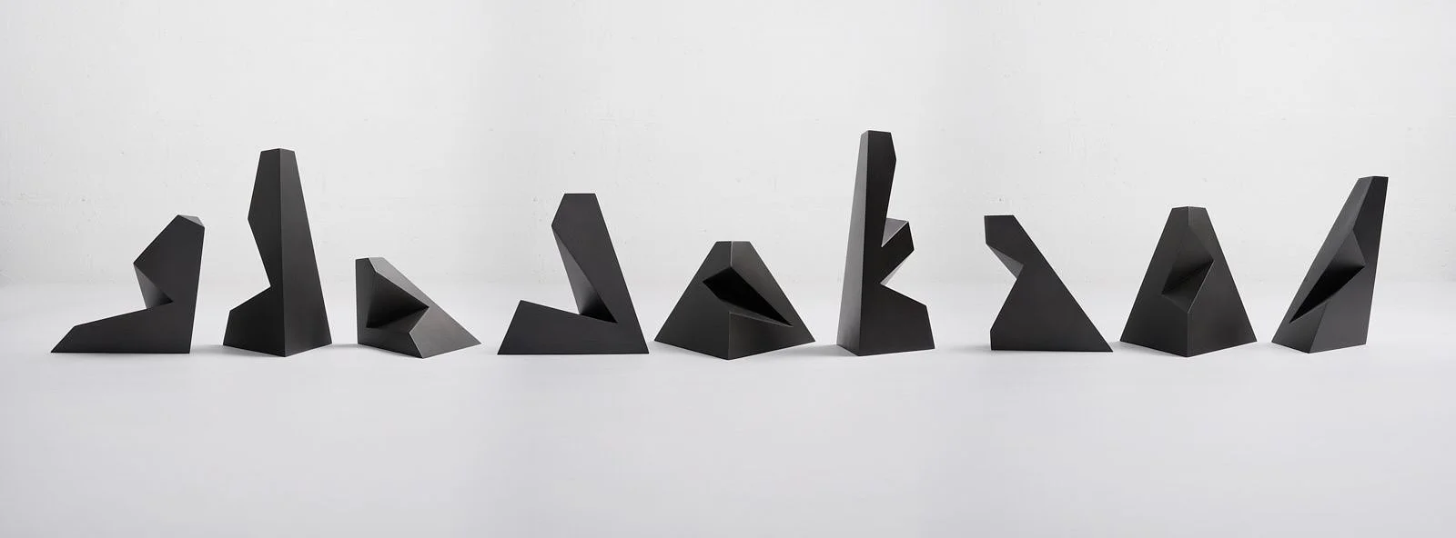 A series of black abstract sculptures with geometric shapes positioned on a neutral background.