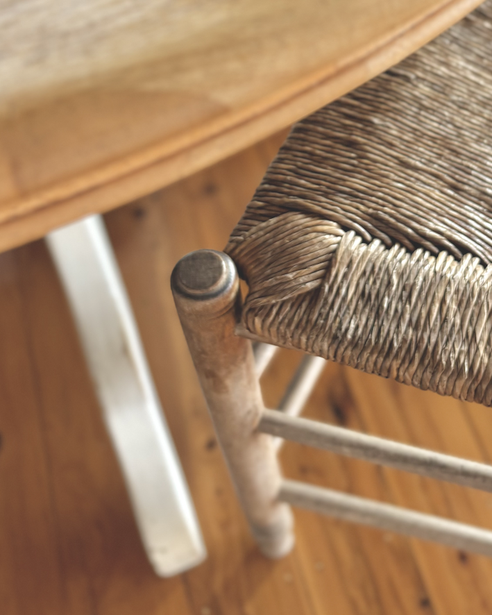 Antique rush-seated chair beside a round timber table on pine floorboards — a close detail of craft and texture in interior designer Olivia Munroe's Newcastle home.
