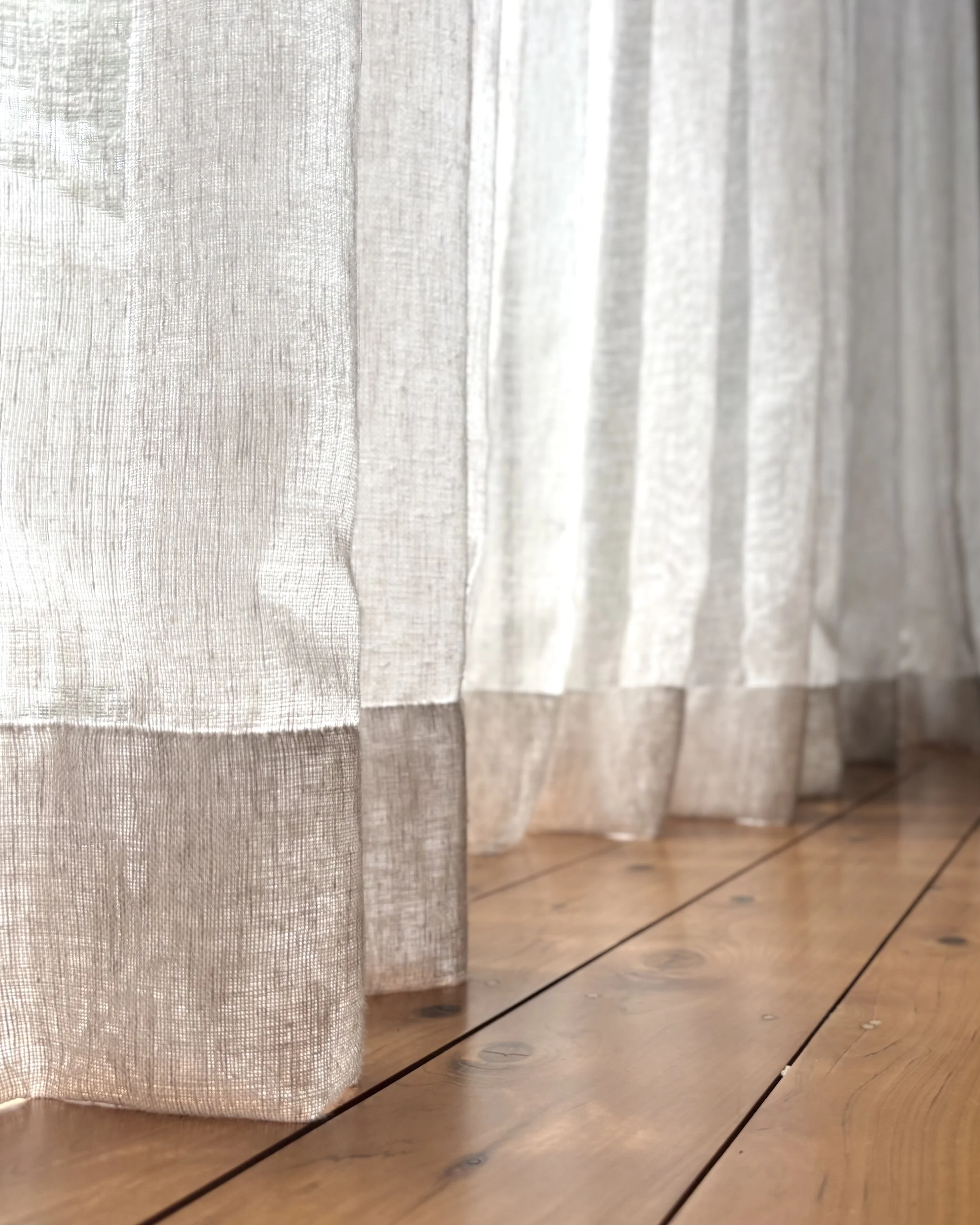 Sheer linen curtains in two tones falling against original pine floorboards — a textural detail from a renovated 1970s home in Newcastle. Natural fibres and soft afternoon light.