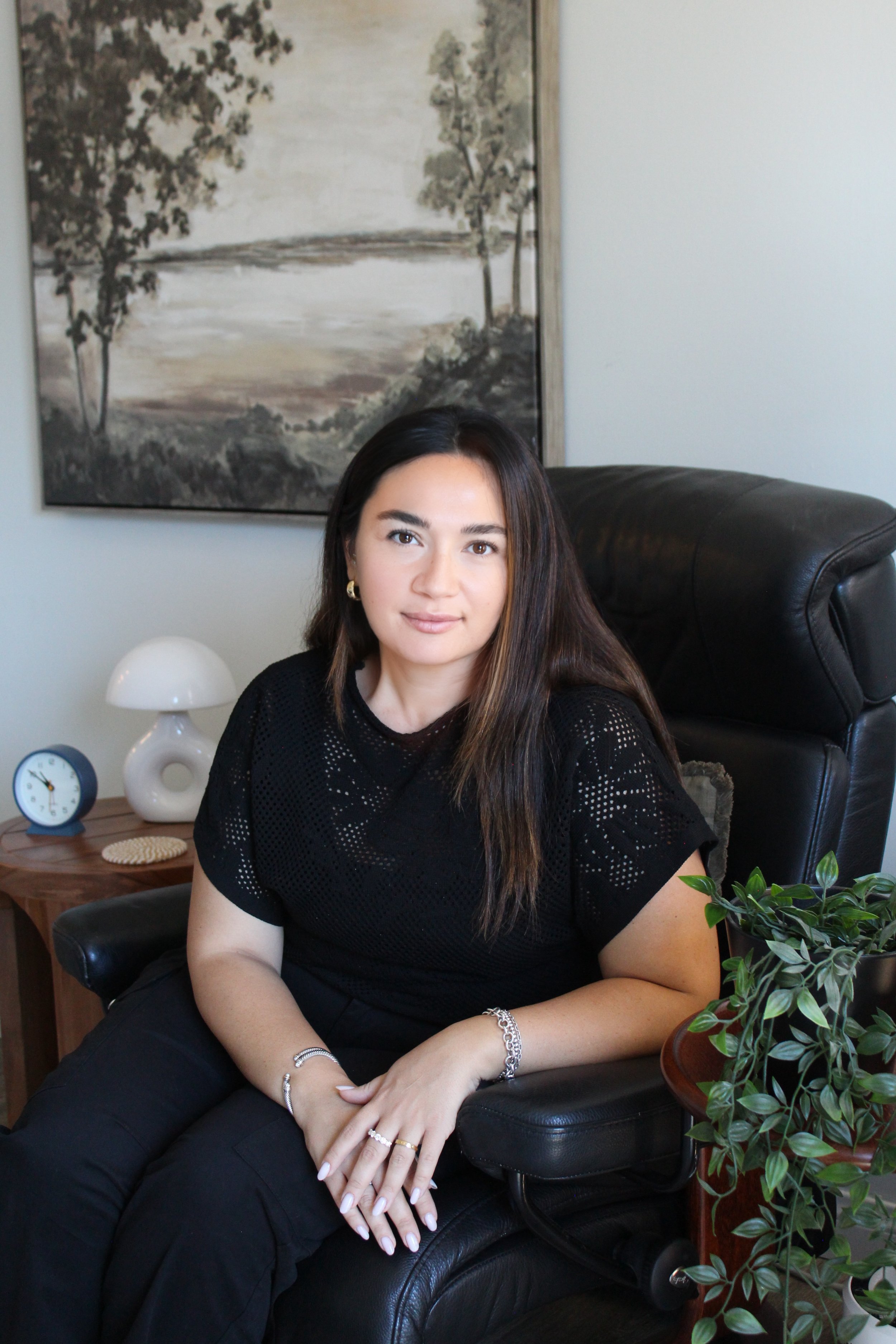 girl sitting smiling softly in chair with plant