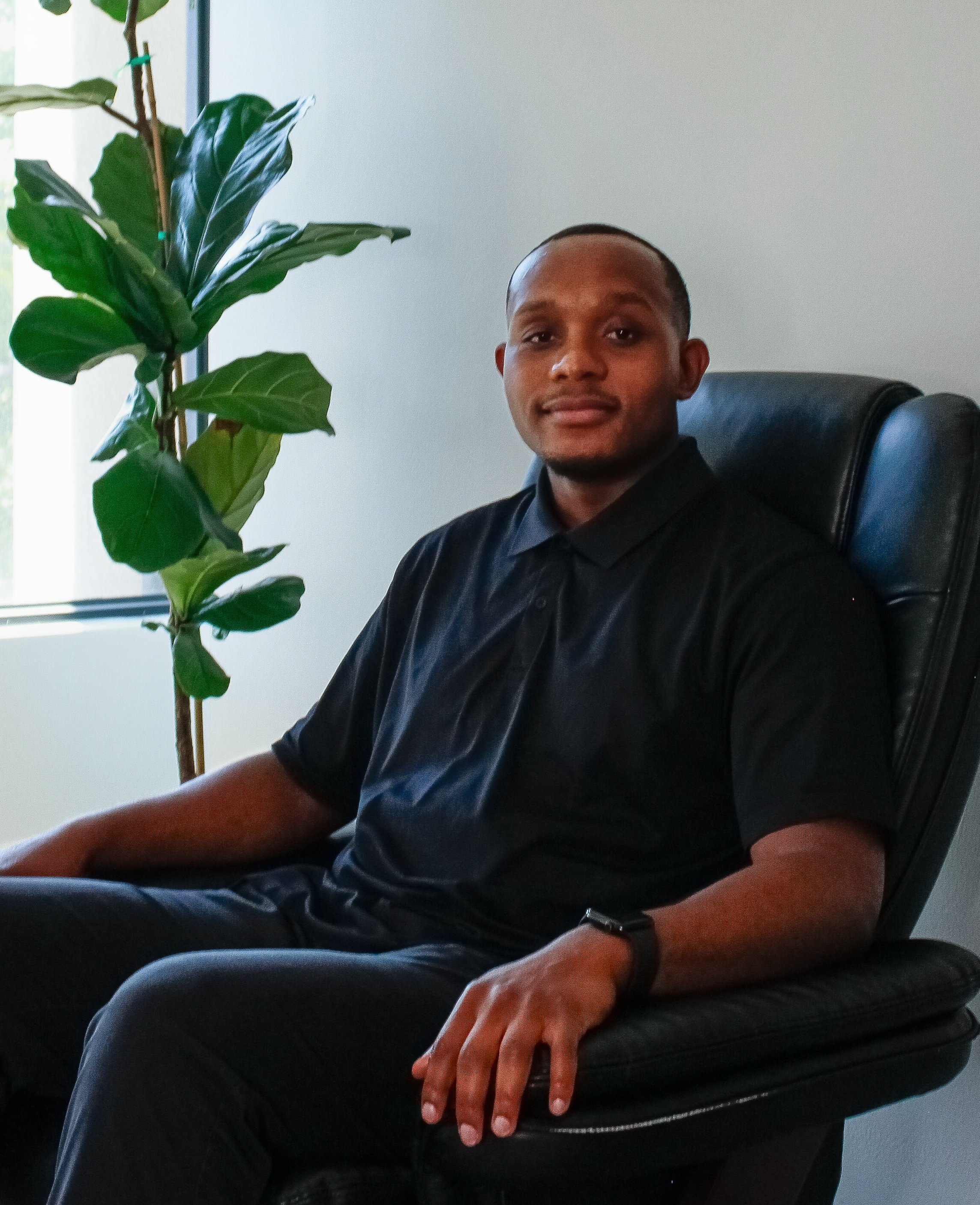 Close-up portrait of a man with short hair, wearing a dark, polka-dotted collared shirt, looking directly at the camera with a neutral expression.