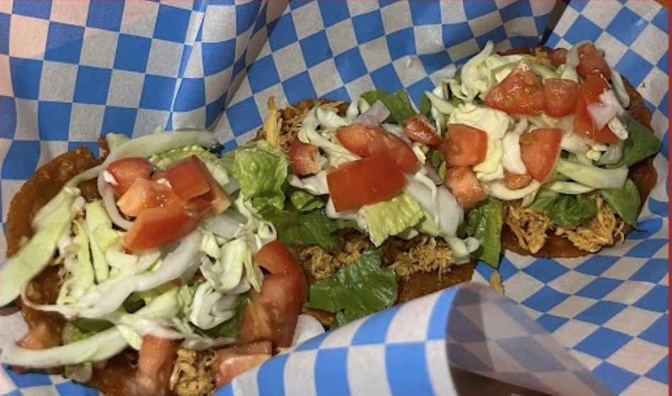 A photo of belizien food, Salutes with shredded meat, lettuce, tomatoes, and onions. It is sitting on a clue and white checked paper.