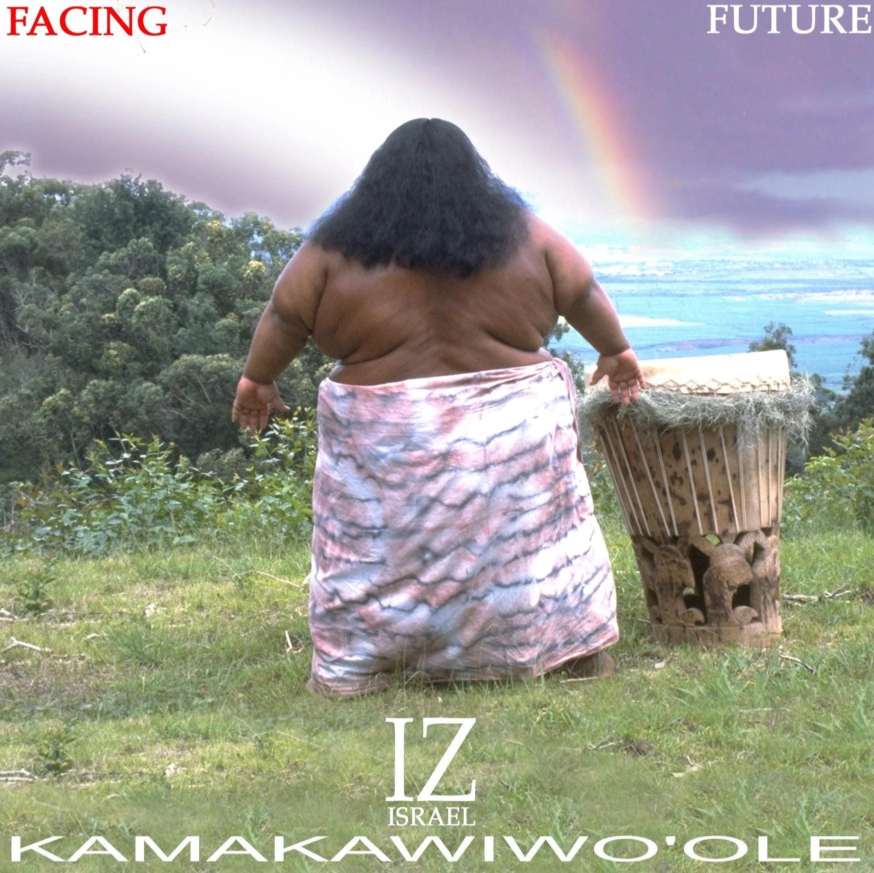 A large, shirtless Hawaiian man with long dark hair standing outdoors on a grassy hill, looking at a rainbow in the sky, with lush trees in the background. He is wearing a pink and white patterned skirt and standing next to a traditional pahu drum.