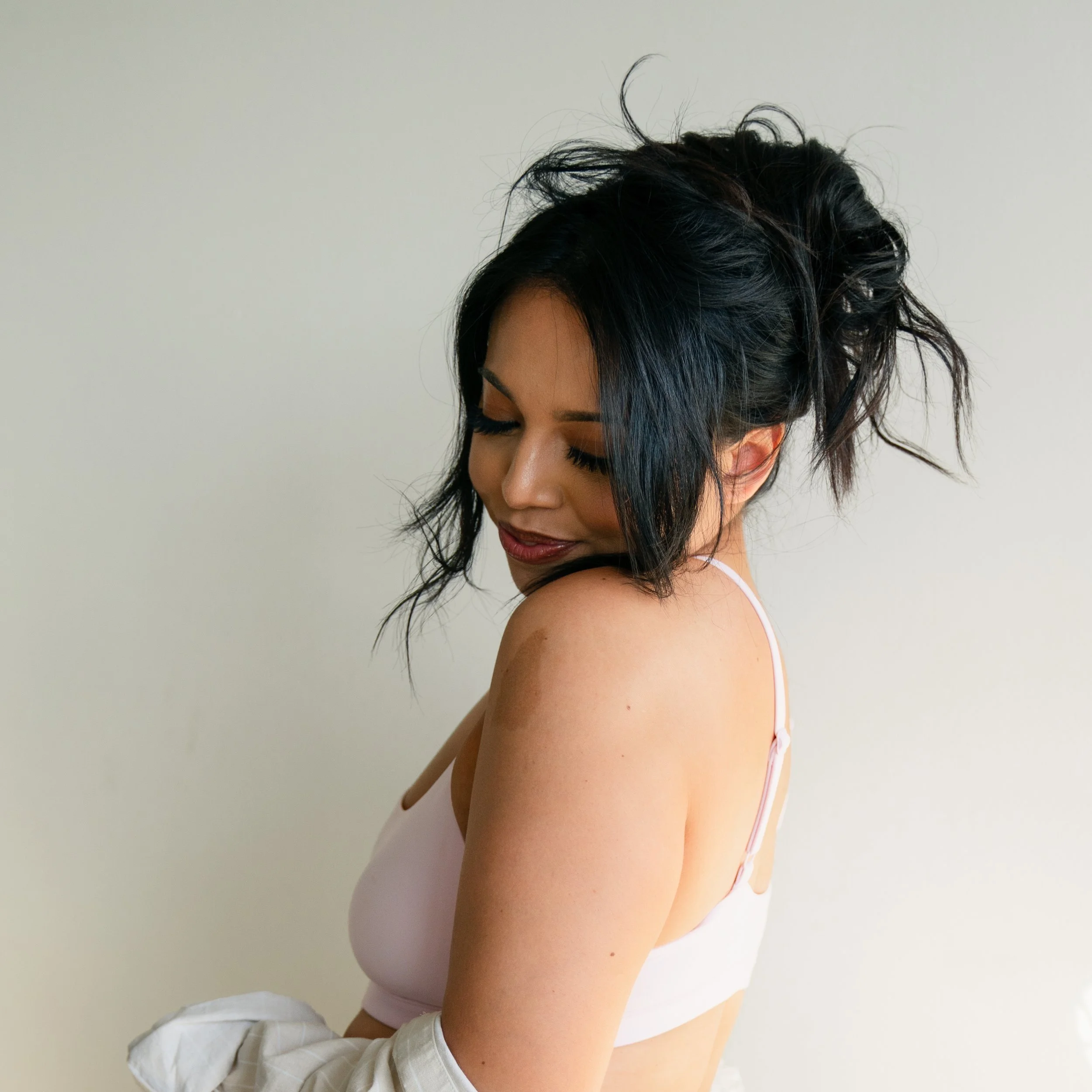 Woman with dark hair styled in an updo wearing a light-colored tank top and posing against a plain background.