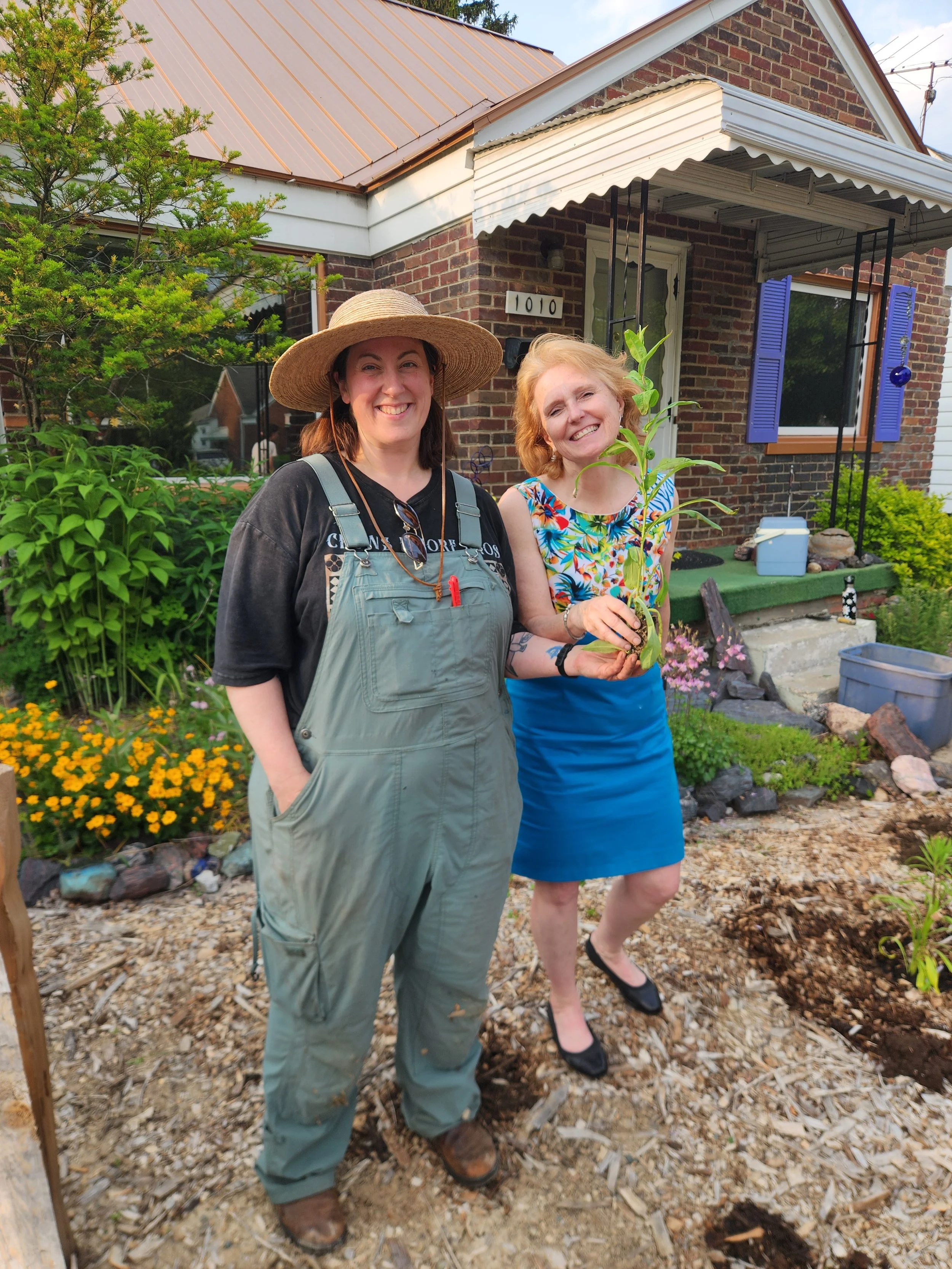 Two people smiling in front of a home with a native plant