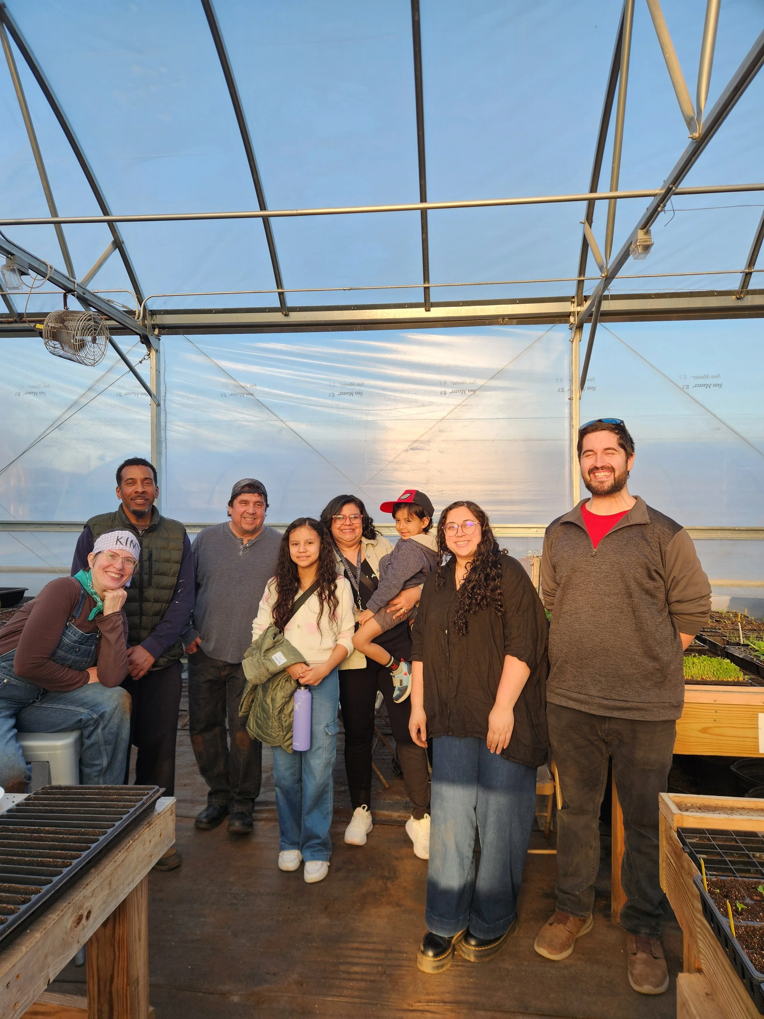 Group of garden club members in the greenhouse with seeding trays. Adults and kids.