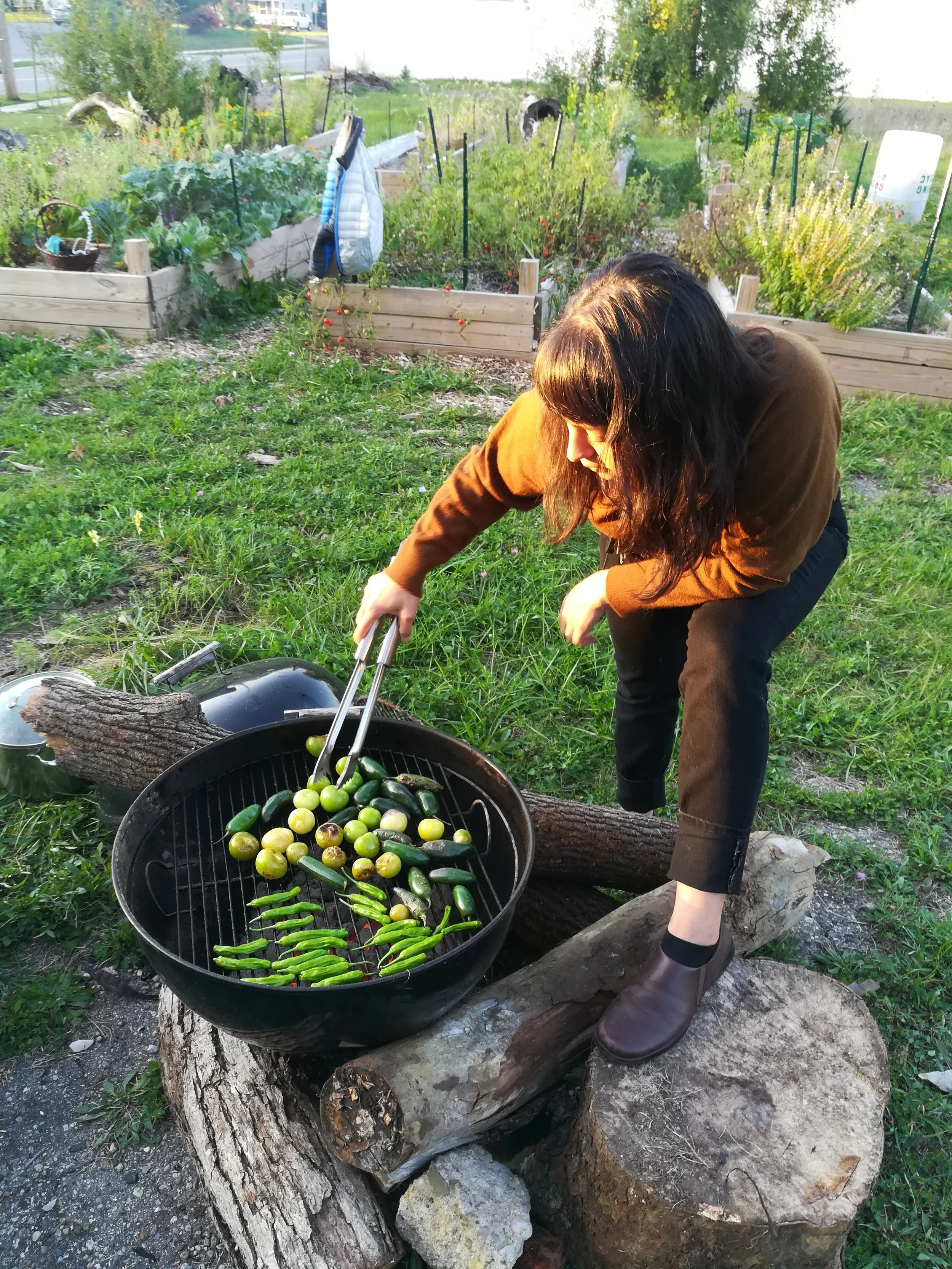 Person in yellow jacket poking veggies on a grill with tongs.