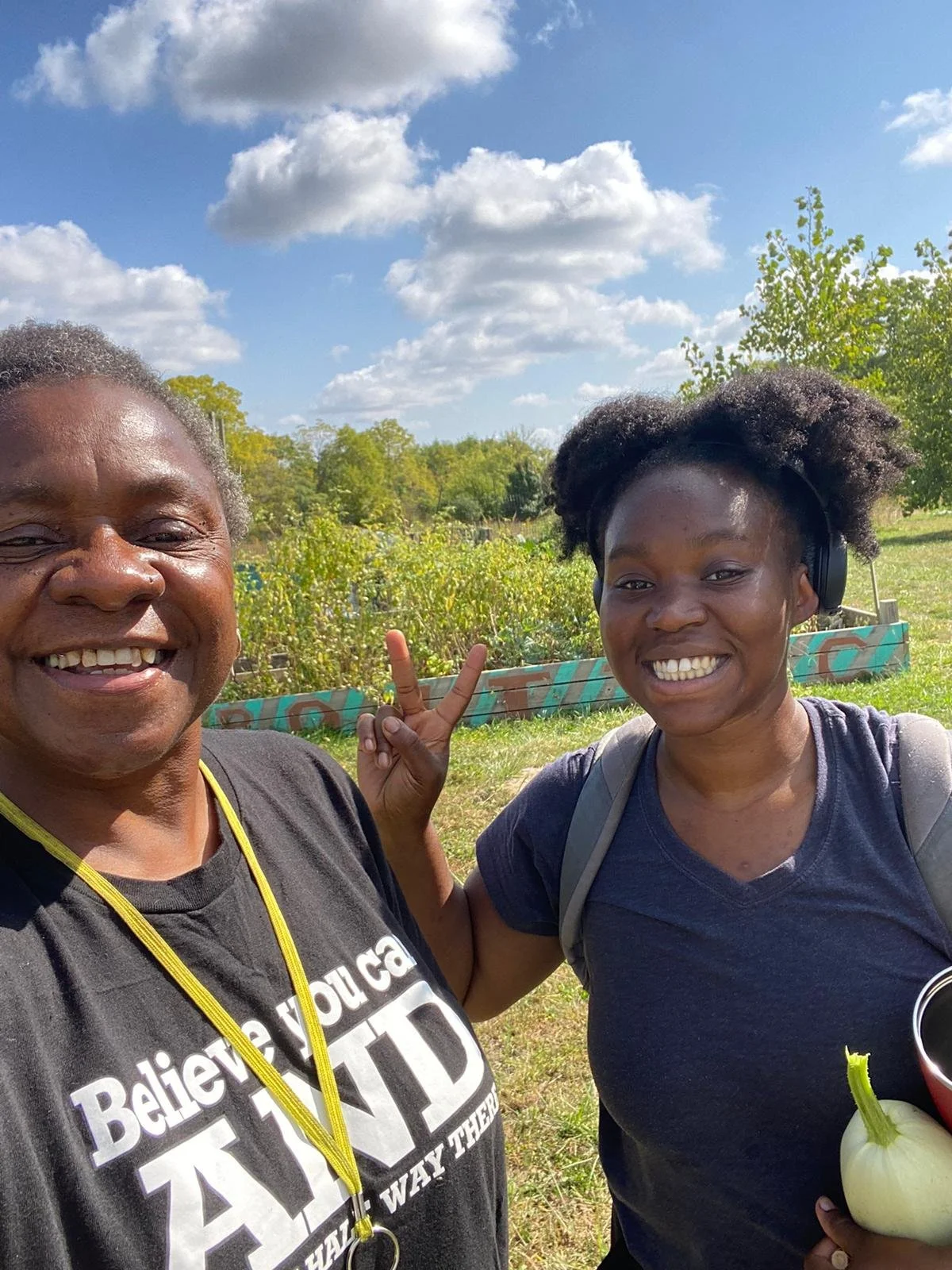 Two people smiling, one holding a piece sign.