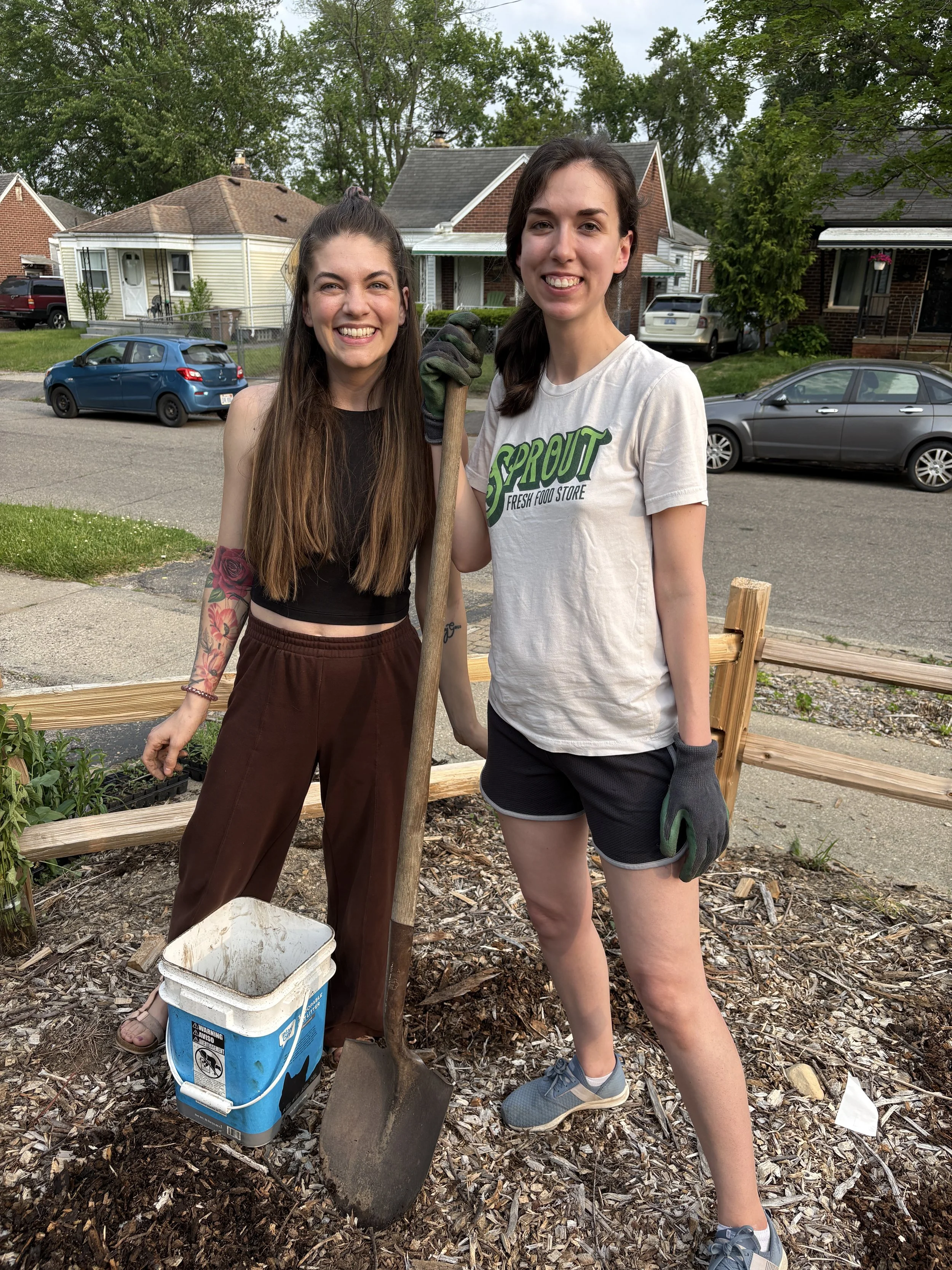 Two people smiling, holding a shovel, and spreading woodchips.