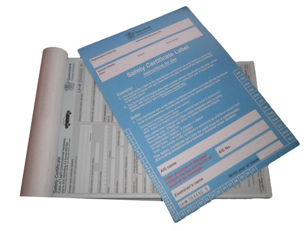 A safety certificate label printed on a blue sheet of paper resting on top of a rolled-up document.