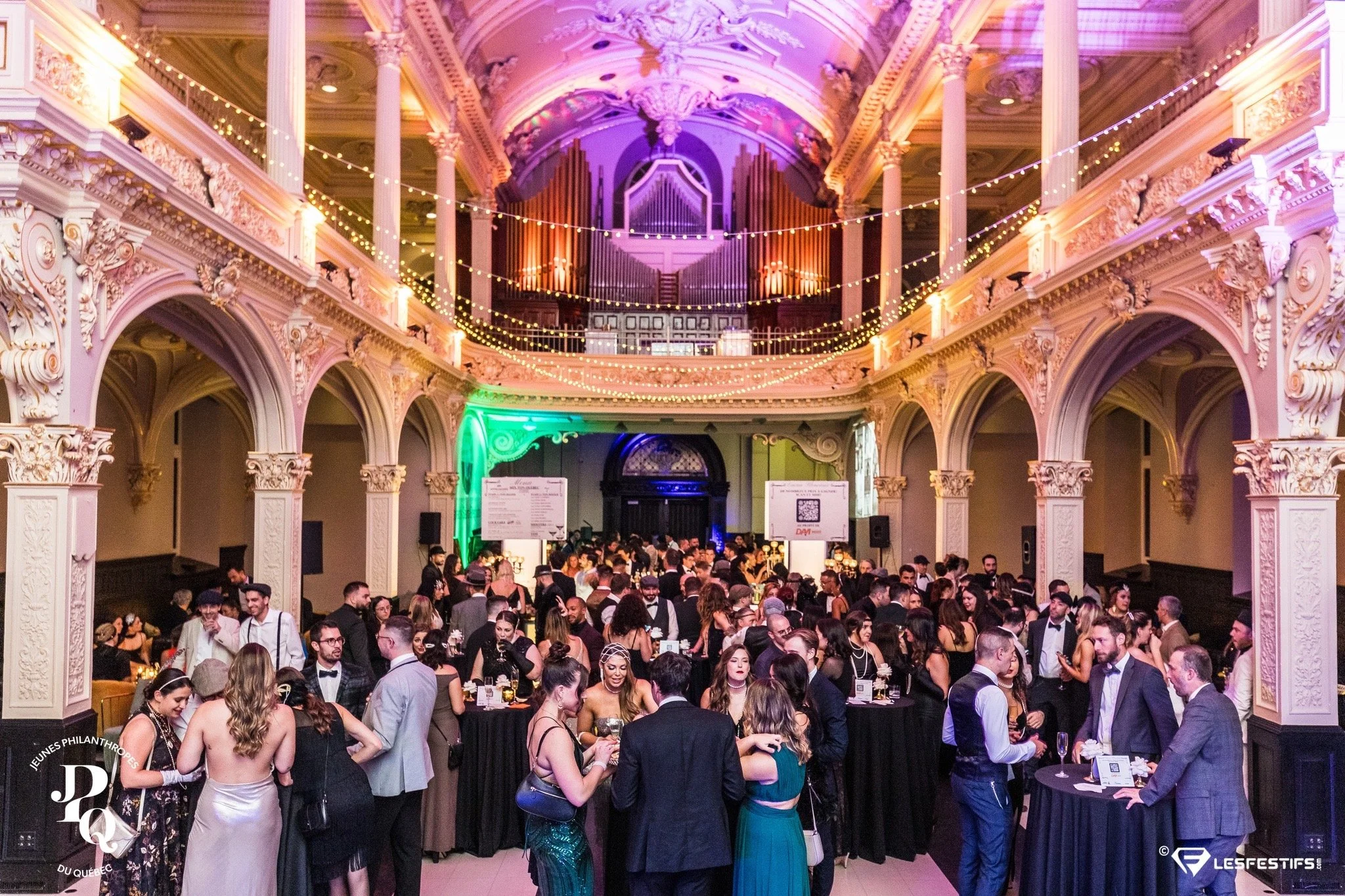 Salle de bal élégante avec invités en tenue de soirée, lustres décoratifs, piliers ornés et lumière tamisée.