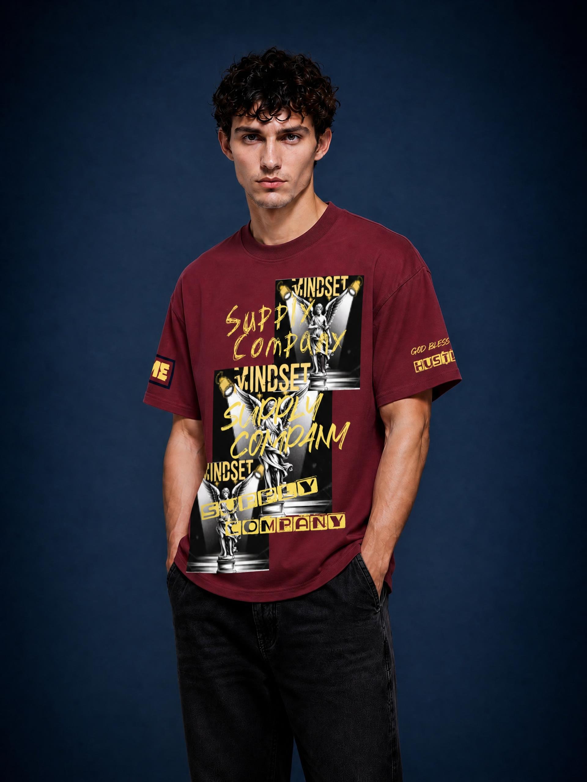 Young man with curly dark hair and wearing a maroon T-shirt with bold graphic print, standing against a dark blue background.